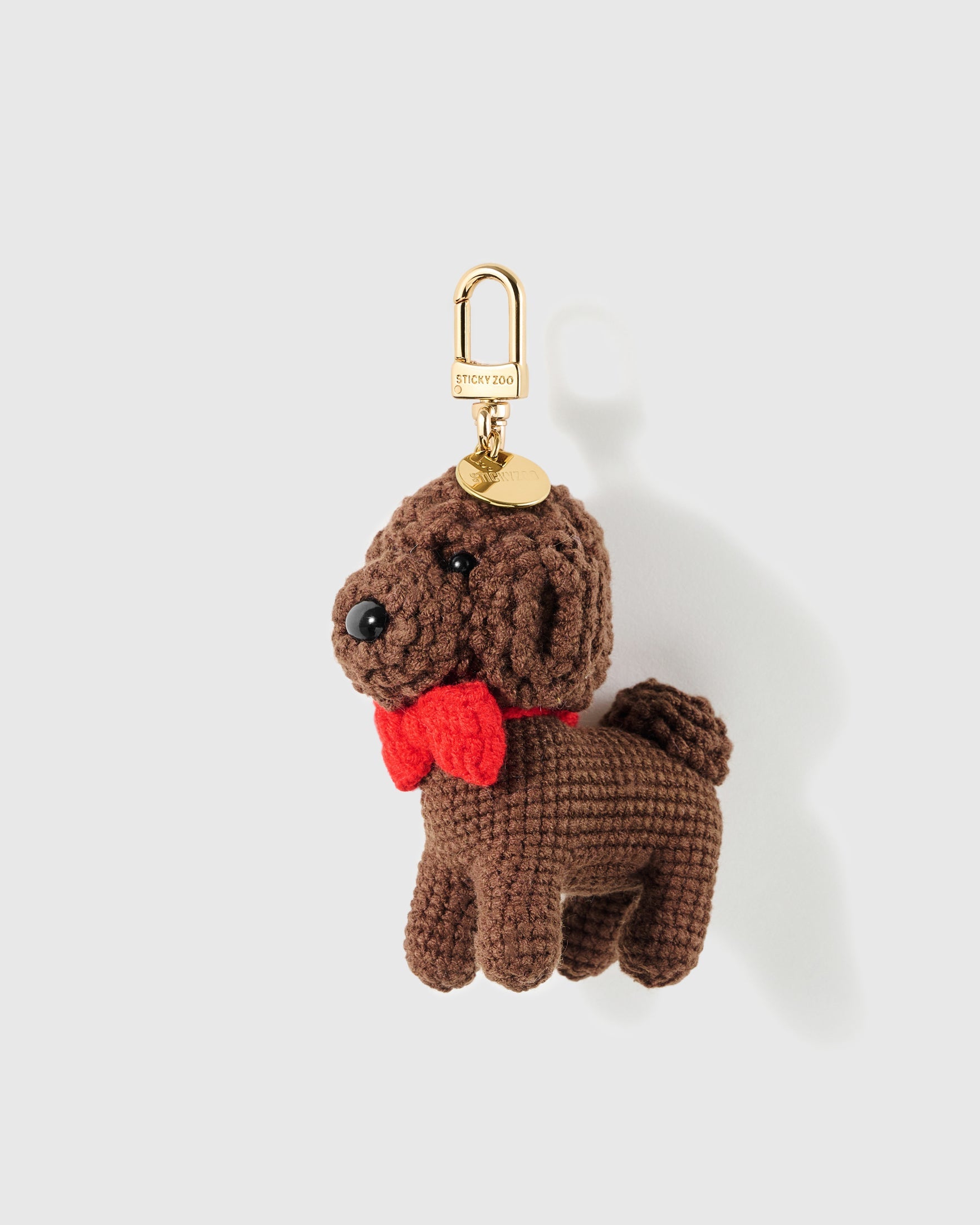 Red Bow Poodle Crochet Charm with curled crochet texture shapes the ears and coat while the bright bow brings one clear colour accent on a light background