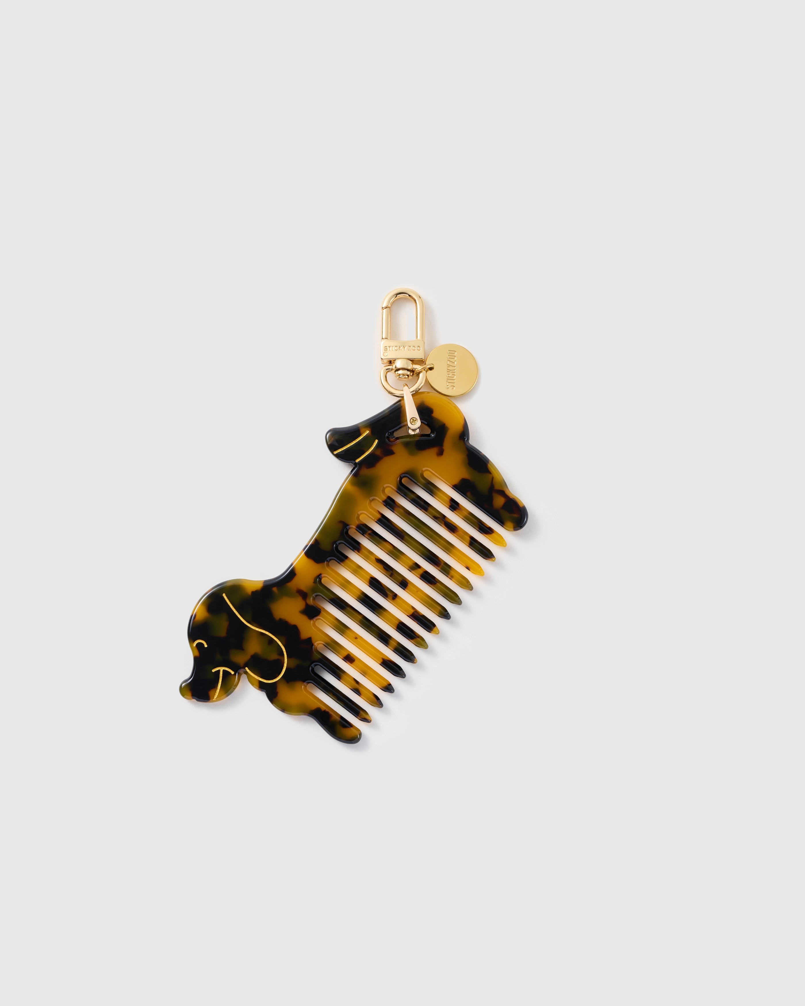 STICKYZOO Simone Dachshund Comb Charm with an amber-and-black tortoiseshell-pattern body, built-in comb teeth, fine gold-tone details and gold-tone clip