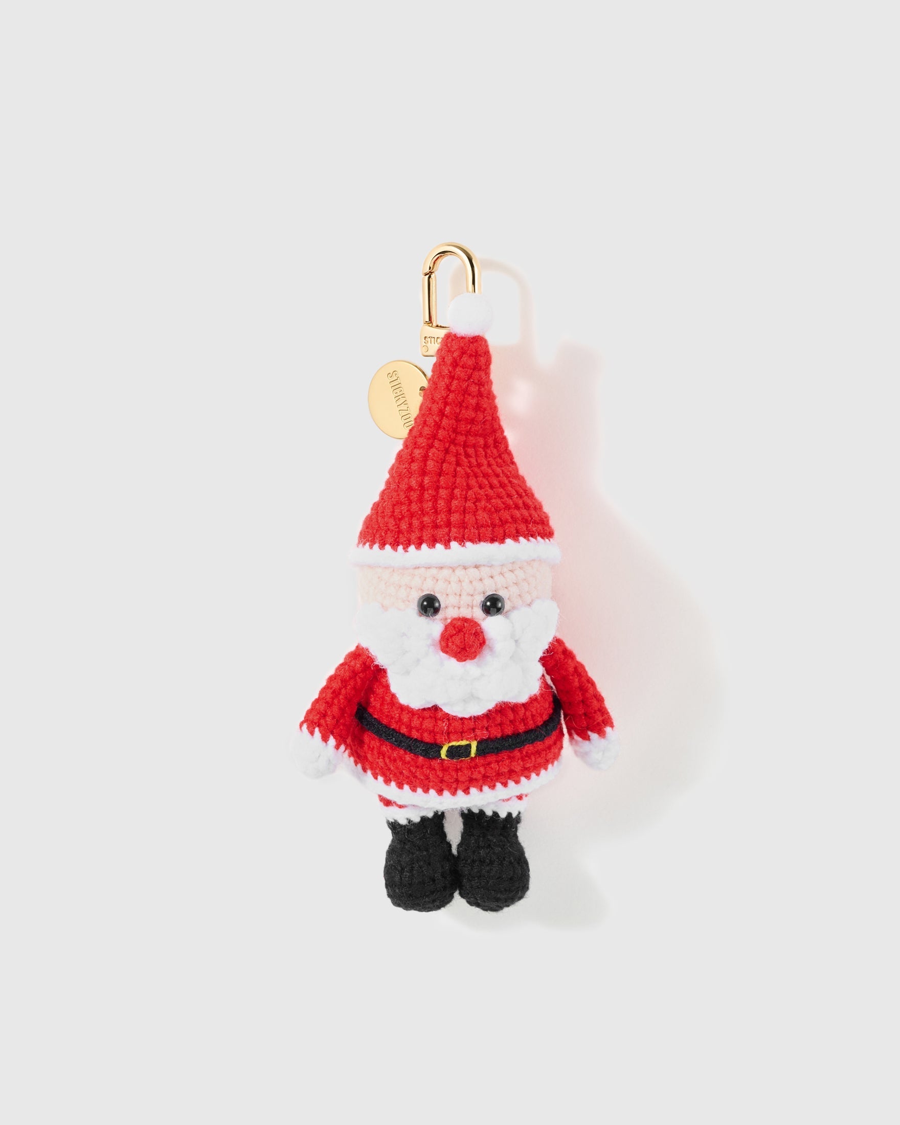 Classic Santa Crochet Charm with a tall red hat, white beard, black boots and tiny belt are worked into the crochet figure on a light background