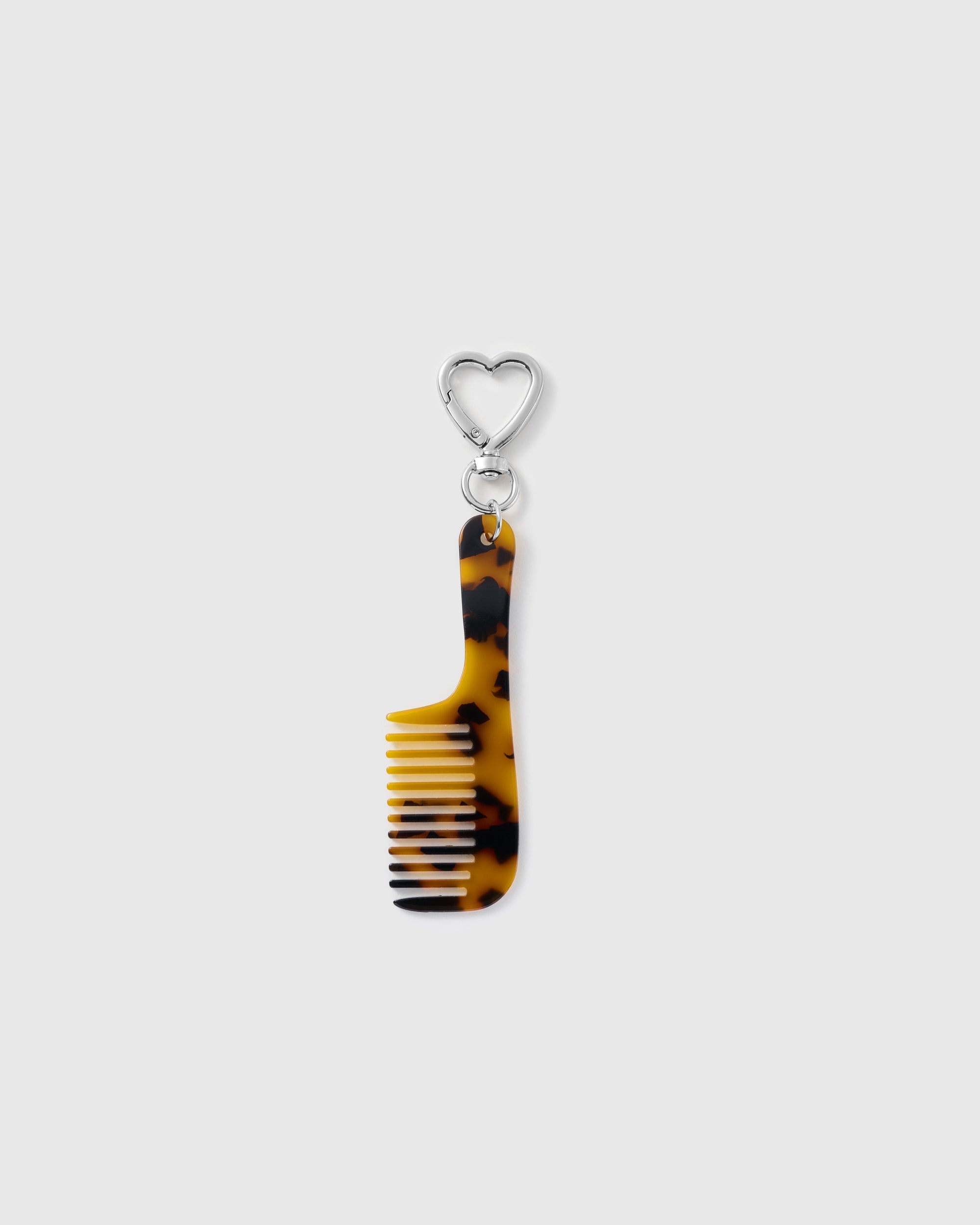 STICKYZOO Audrey Pocket Comb Charm with a long amber-and-black tortoiseshell-pattern handle, built-in comb teeth and silver-tone heart clasp