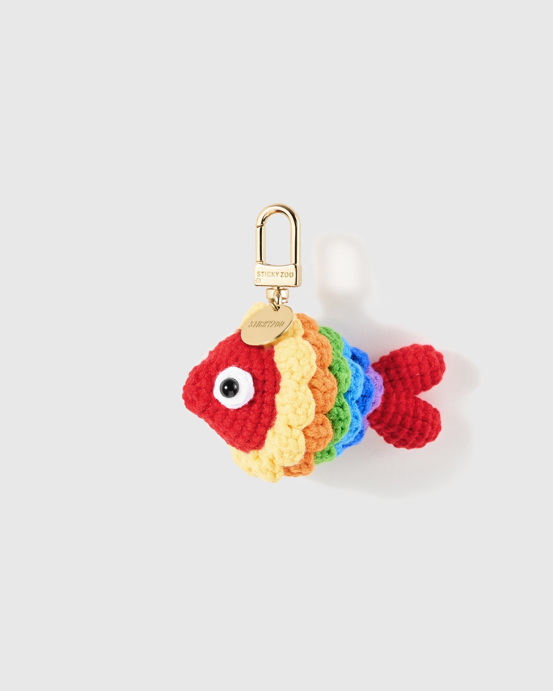 Rainbow Fish Crochet Charm with rows of red, orange, yellow, green and blue yarn build the fins and striped body on a light background
