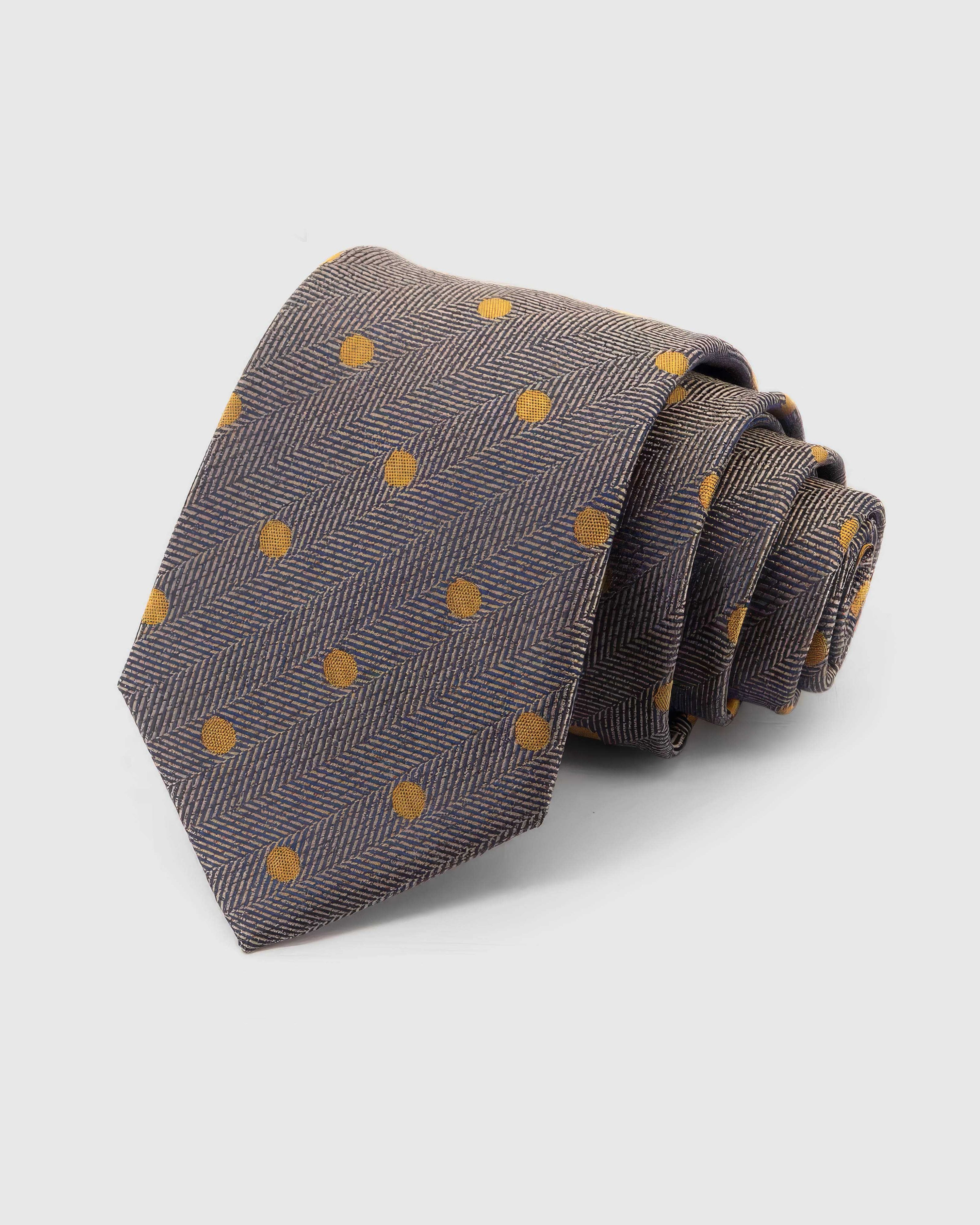 STICKYZOO Pewter Herringbone Dot Tie rolled on white, showing a pewter and charcoal herringbone field punctuated by small mustard-gold dots across the front blade.