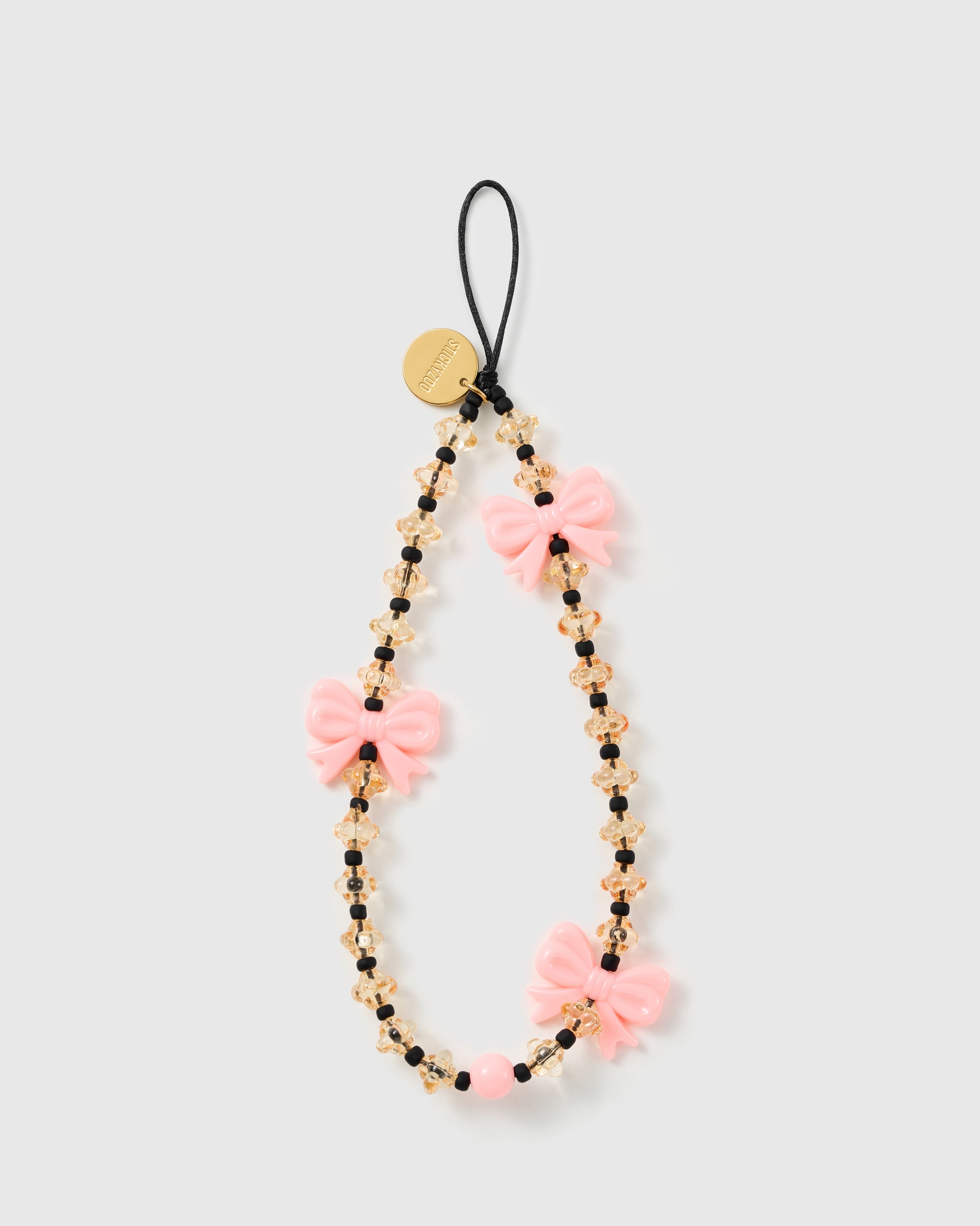 STICKYZOO beaded phone strap laid flat, three glossy pink bows along faceted honey beads with black spacers and a gold-tone disc