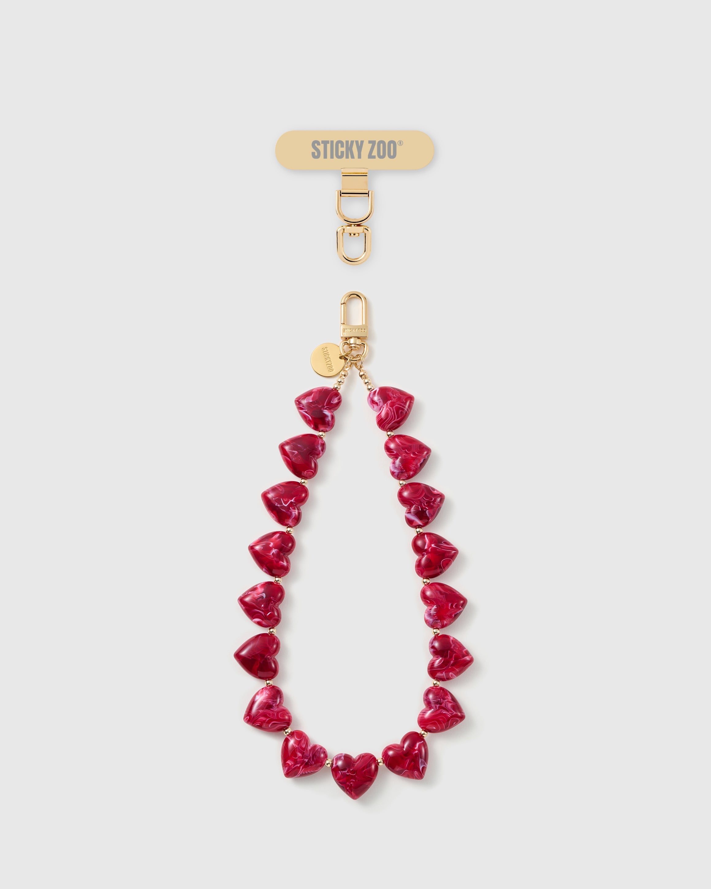 Ruby-red marbled heart bead phone strap with an 18K gold-plated hook, STICKYZOO card connector and engraved disc, strung as a wrist loop.