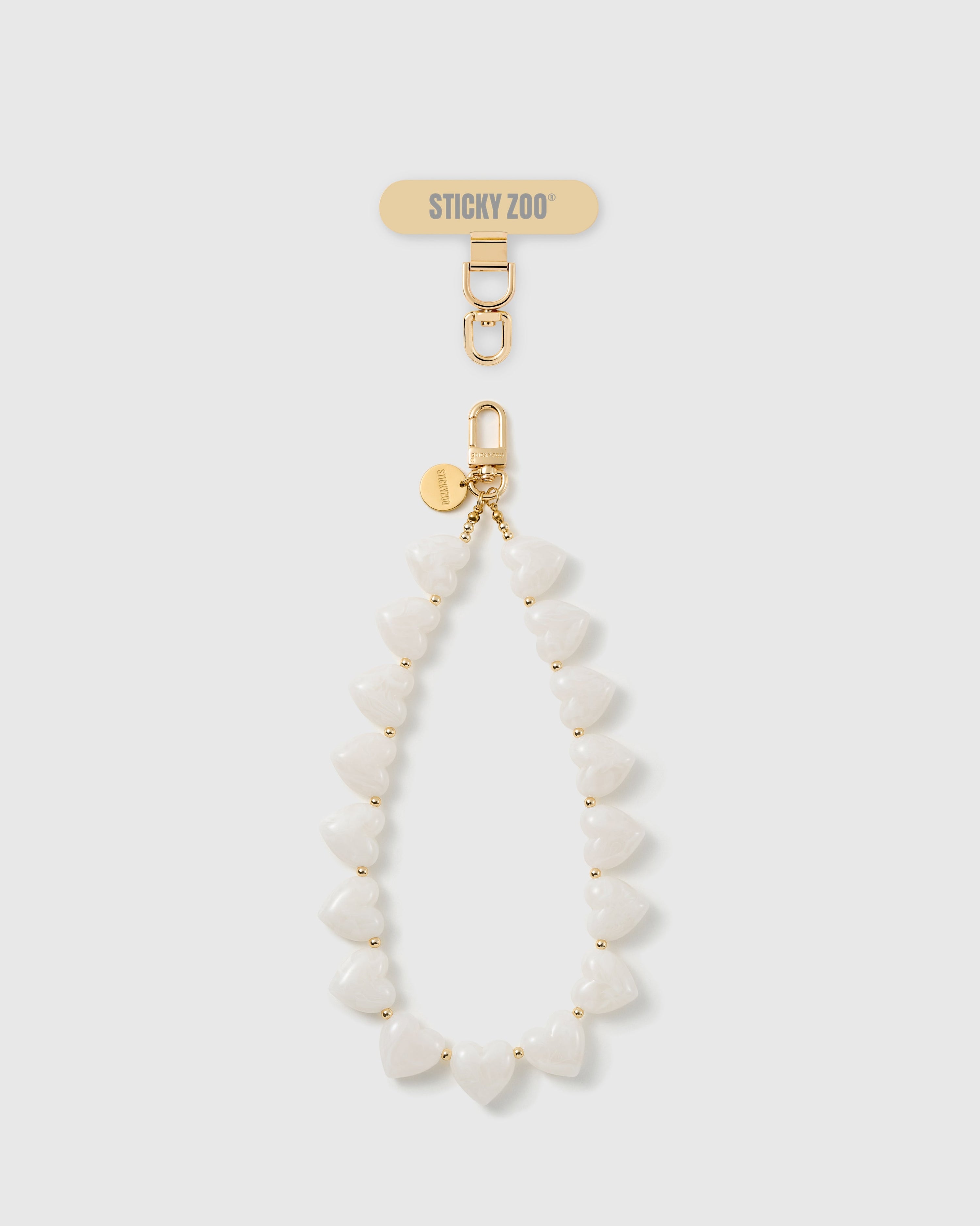 STICKYZOO Coconut Heart phone strap: full strand of milky white heart beads with gold-tone spacers, gold hook and engraved disc, shown on white.