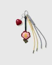 Lucky Money Flower Stack Charm with a heart, money-flower motif, dark-green stem detail and grey-and-yellow cords on a light background