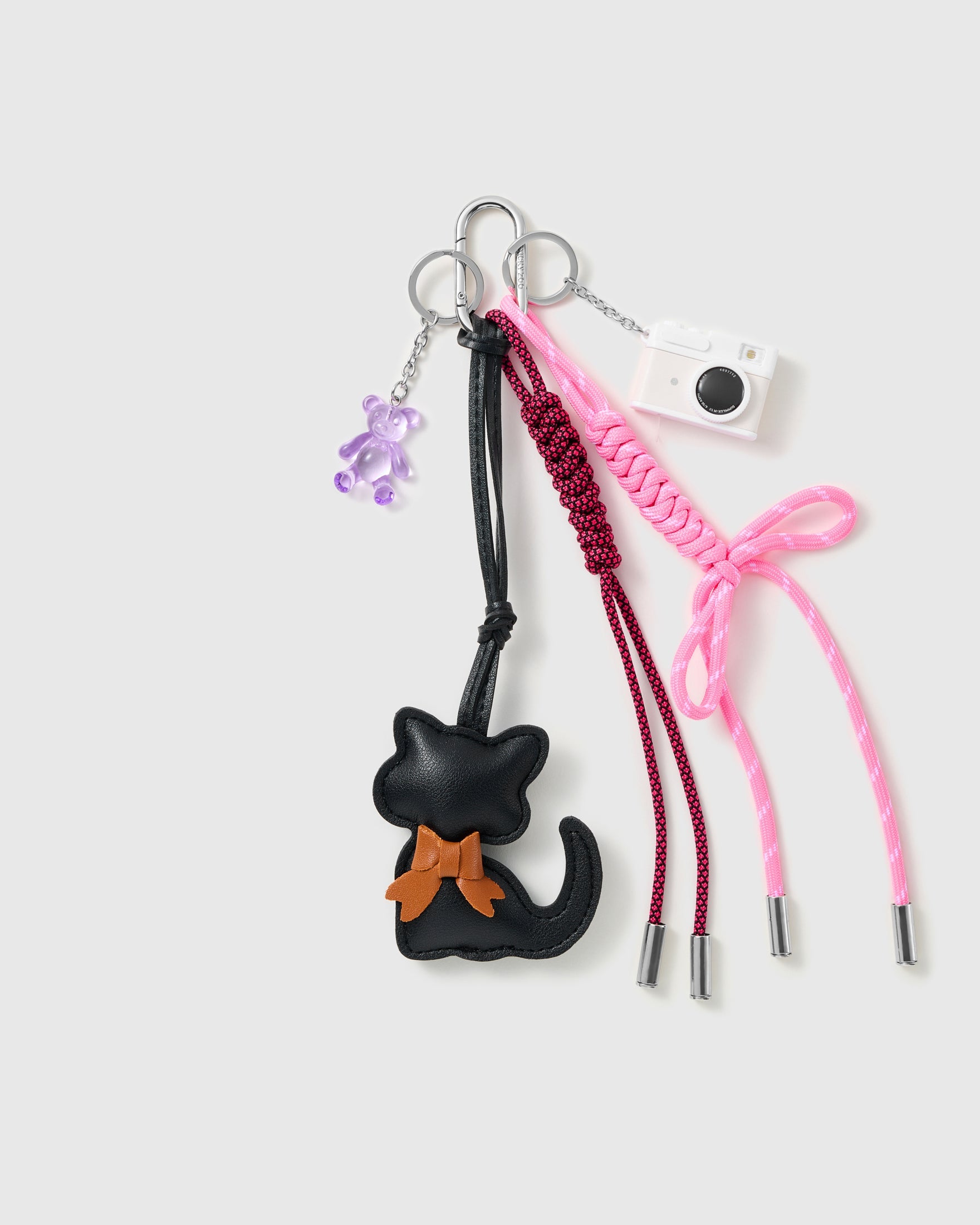 Black Cat Bow Stack Charm with a black cat with brown bow, miniature camera, small purple motif and pink-and-black cords on a light background