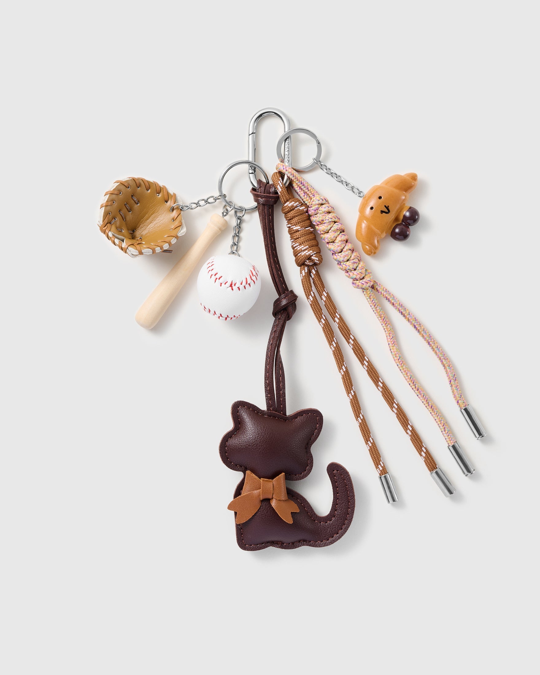 Cocoa Cat Baseball Stack Charm with a cocoa-brown cat with bow, baseball motifs, tiny bear detail and neutral cords on a light background