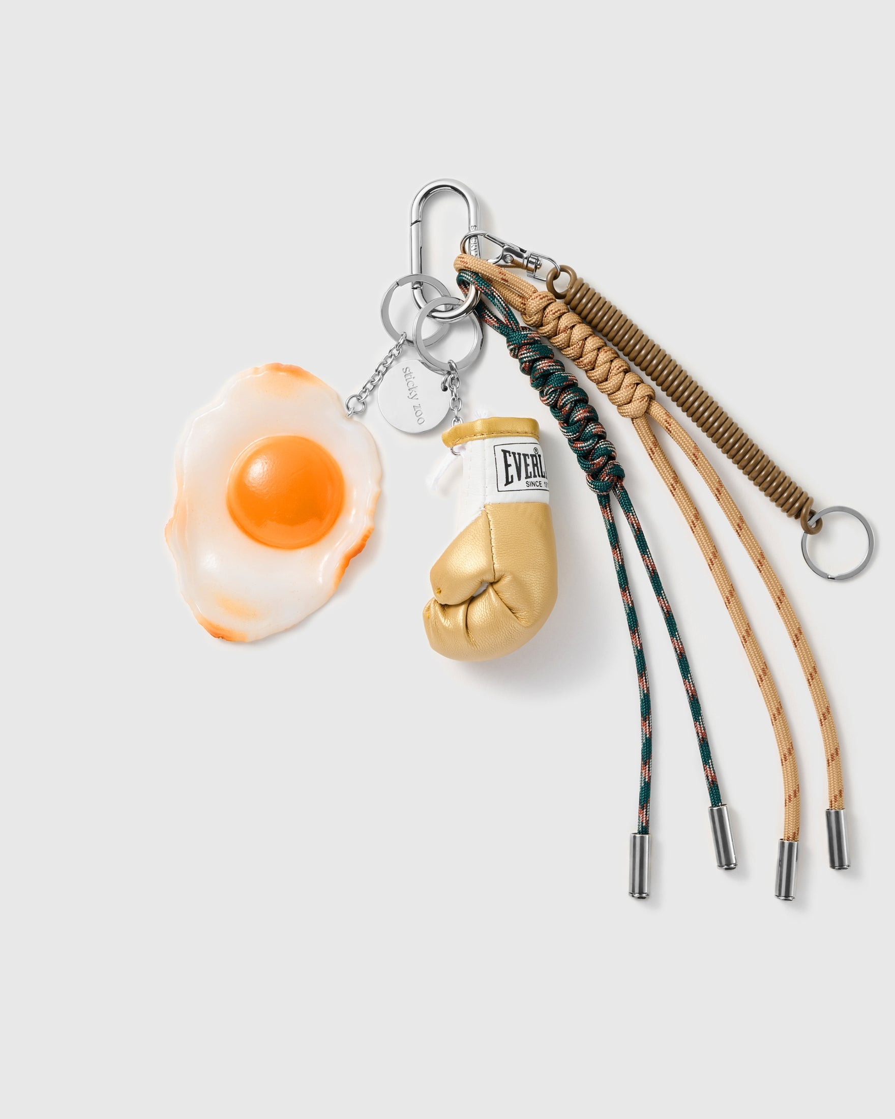 Fried Egg Boxing Stack Charm with a fried-egg motif, boxing glove, stitched label and green-and-brown cords on a light background
