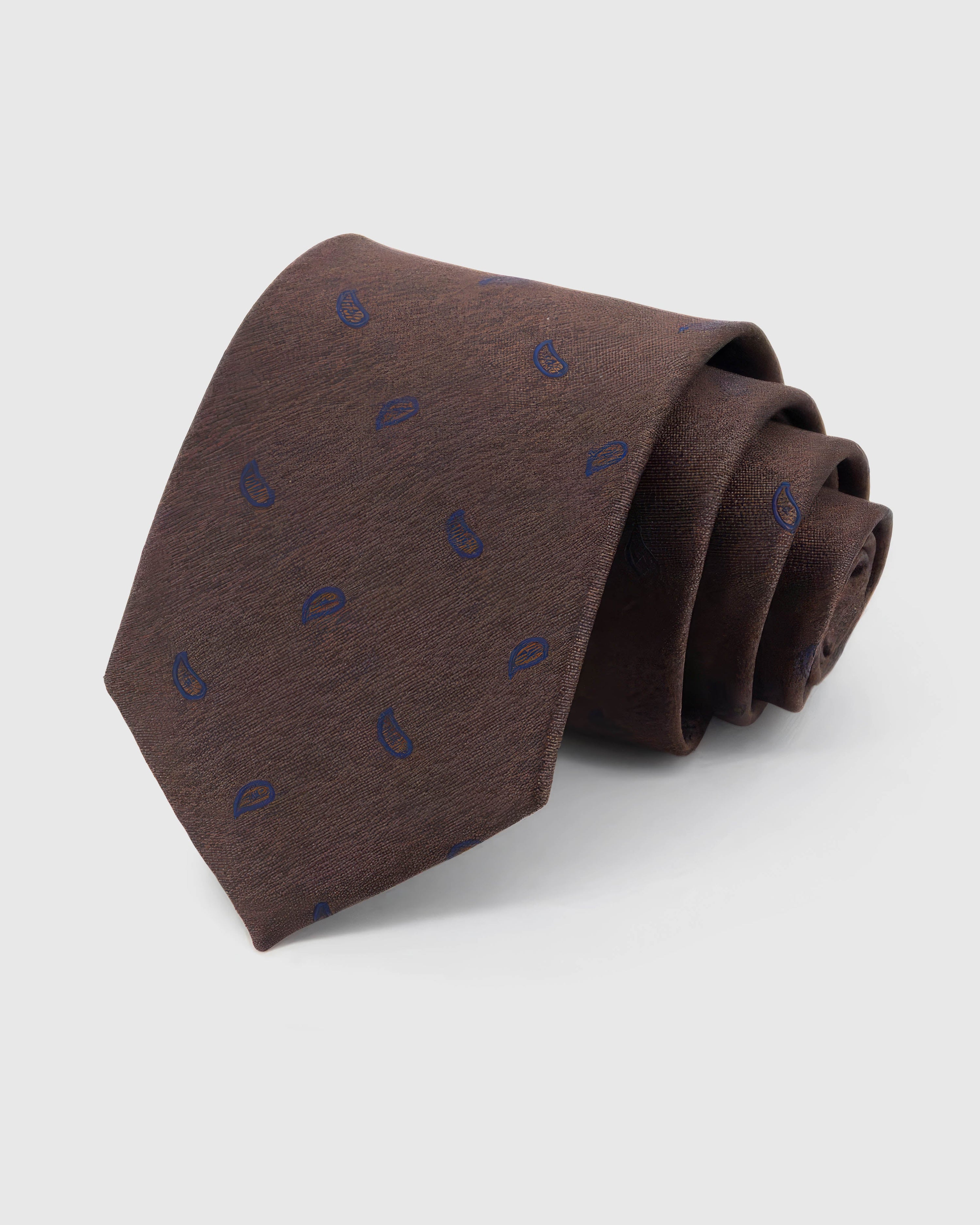 STICKYZOO Espresso Sapphire Paisley Tie rolled on white, showing a textured espresso ground with a compact sapphire-blue paisley repeat across the front blade.