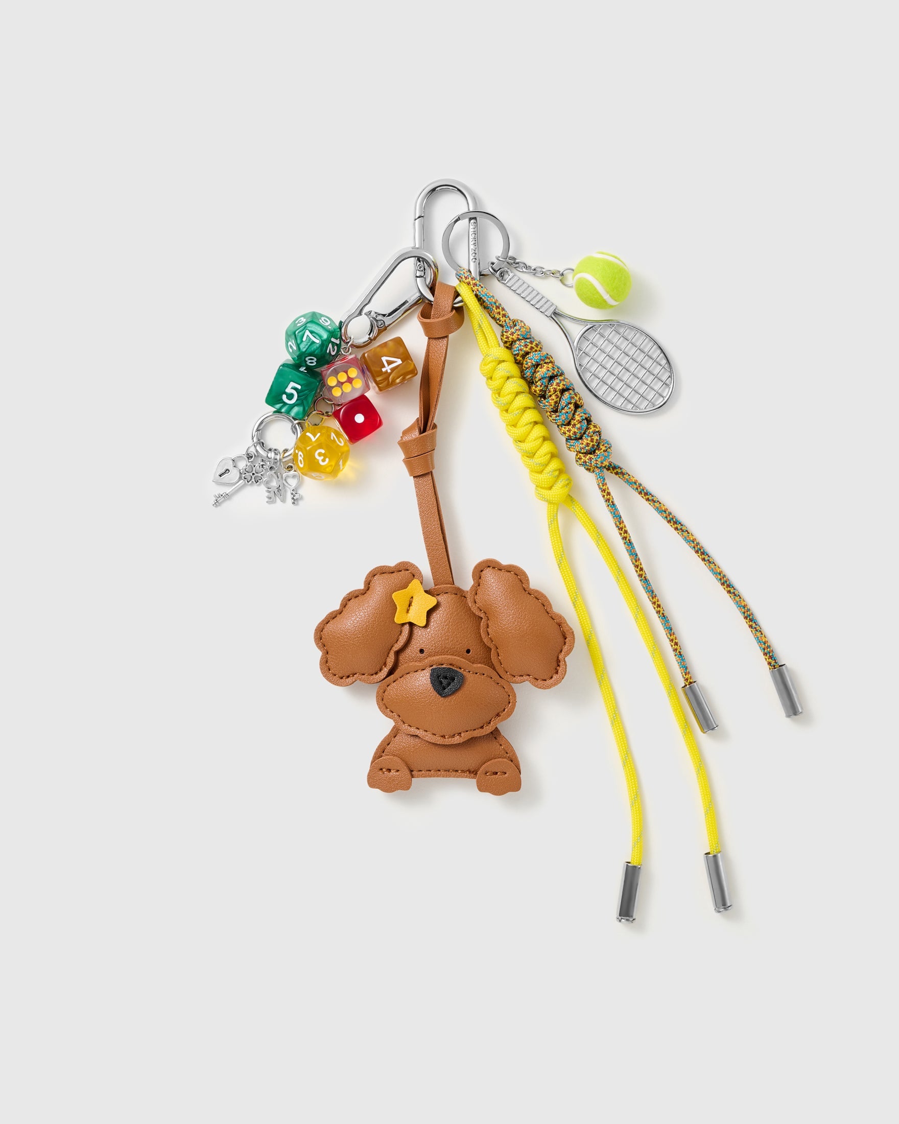 Star Poodle Tennis Stack Charm with a star-glasses poodle, tennis motifs, multicolour blocks and yellow-and-blue cords on a light background
