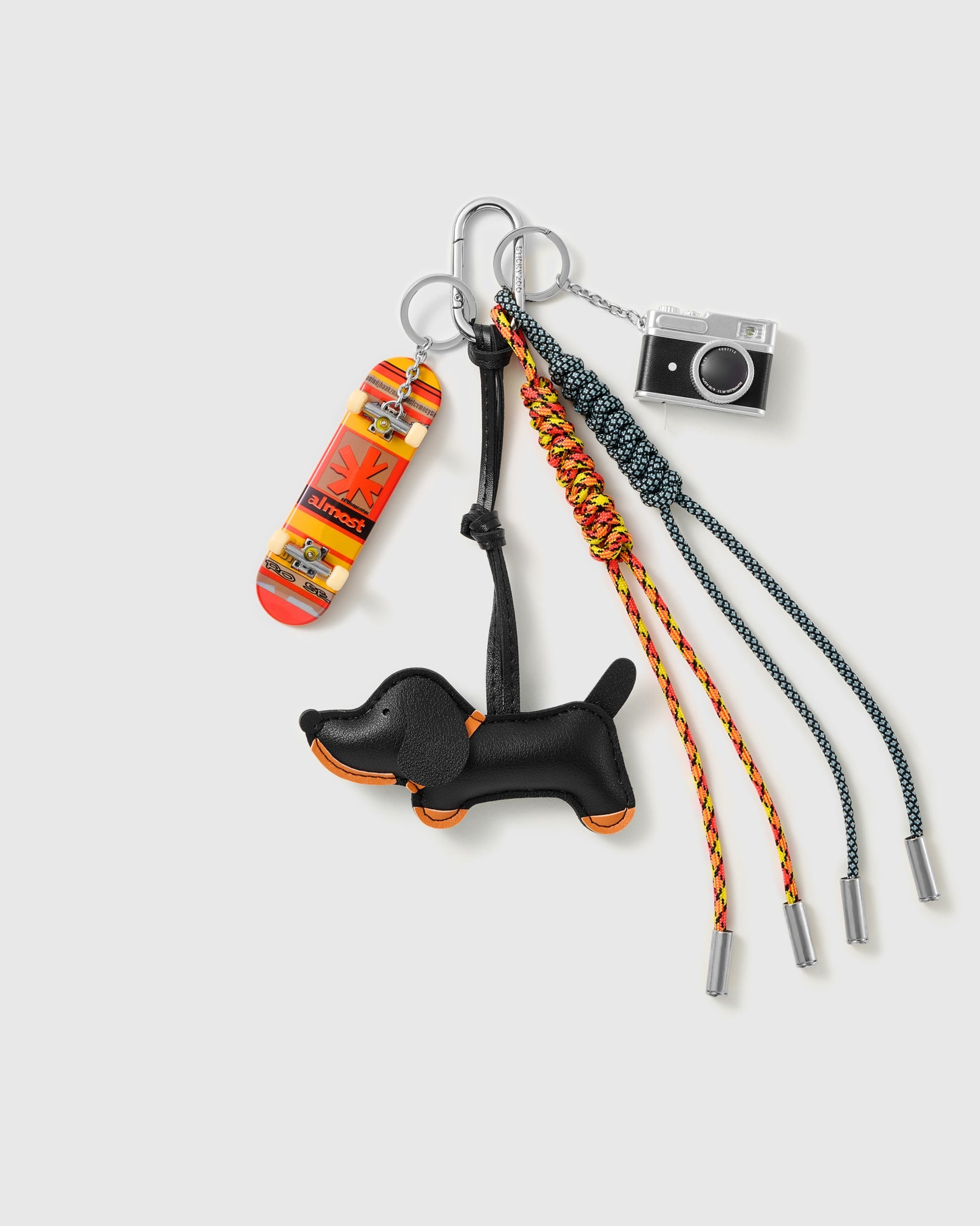 Dachshund Skate Stack Charm with a black dachshund, skateboard motif, miniature camera and orange-and-black cords on a light background