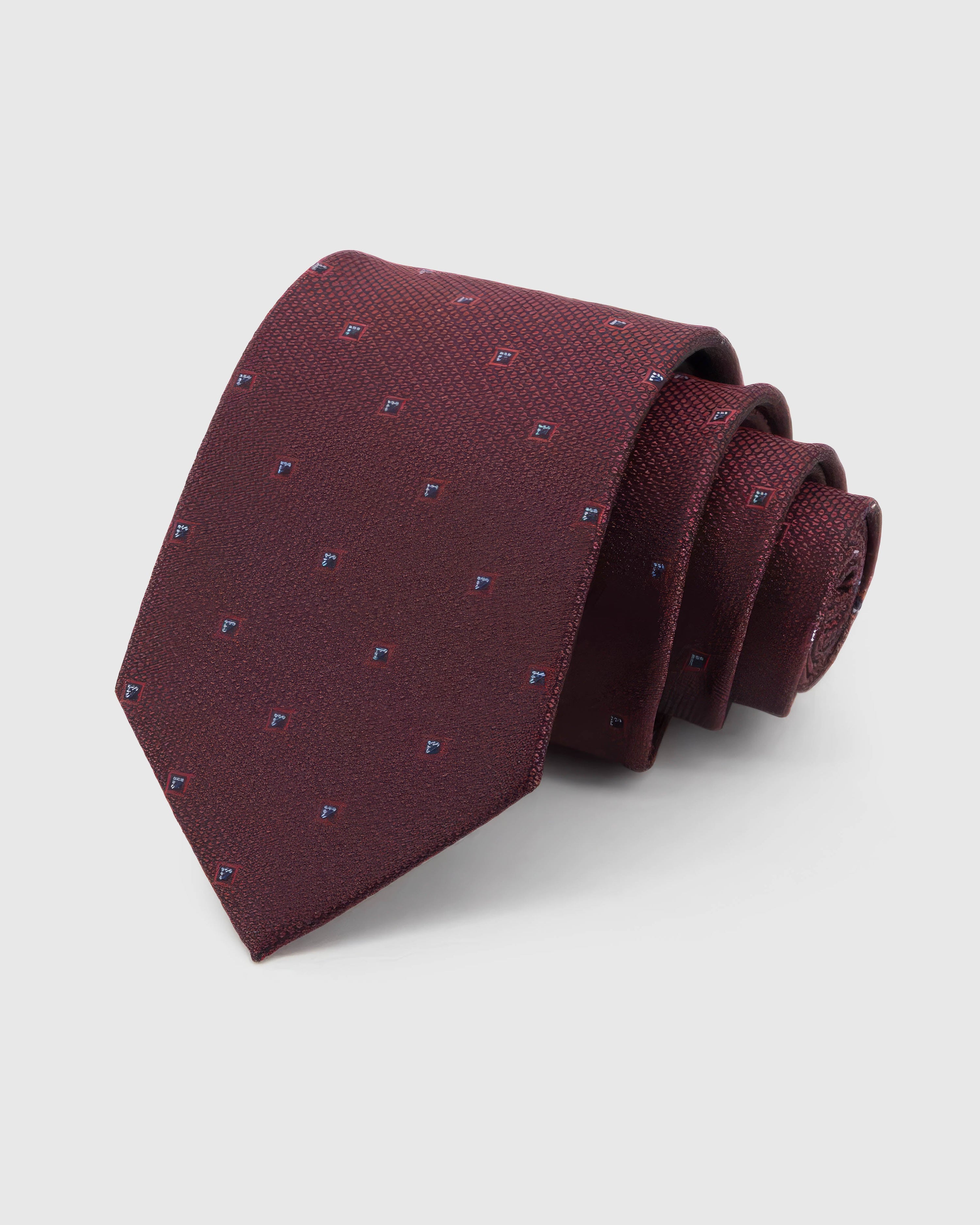 STICKYZOO Garnet Diamond Tie in garnet and ember silk, rolled to show garnet ground with small navy and silver framed diamonds across the blade.