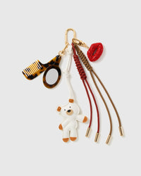 Glam White Pup Beauty Stack Charm with a white pup, tortoiseshell-look glasses, red lips, comb motif and brown cords on a light background