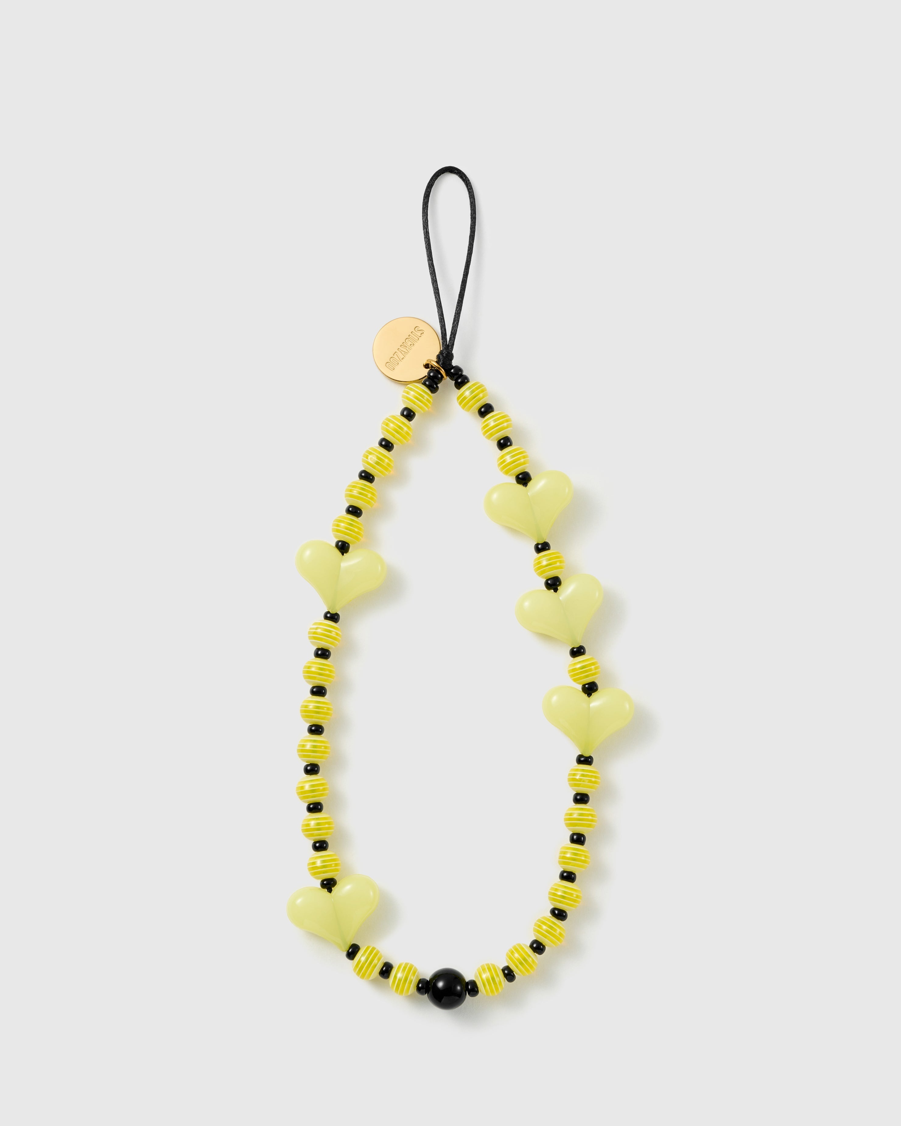 STICKYZOO Lemon Heart phone strap flat: pale yellow glossy heart beads, yellow-and-white striped beads and black spacers on a black cord loop with gold disc