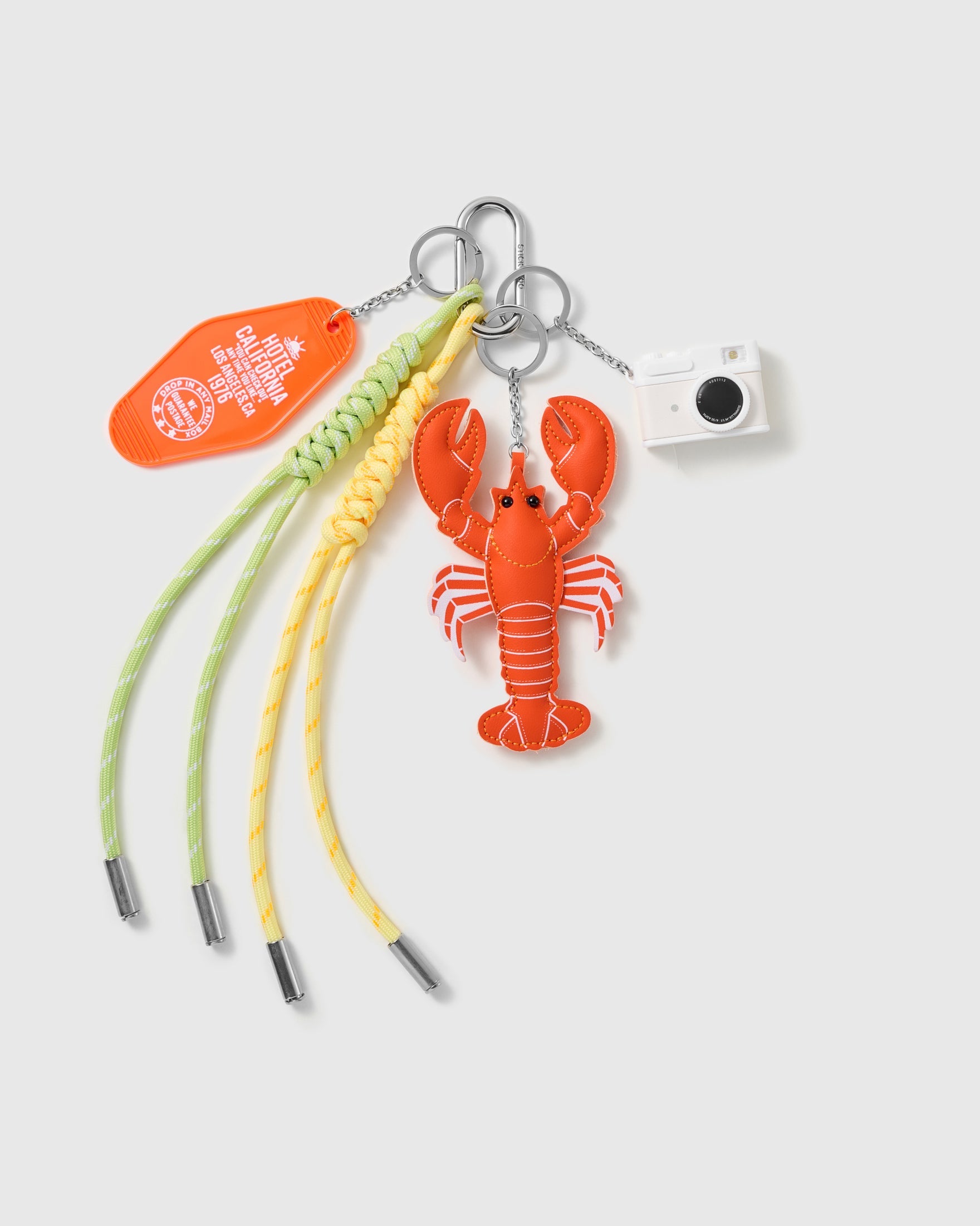Lobster Camera Stack Charm with an orange lobster, miniature camera, stitched tag and yellow-and-green cords on a light background