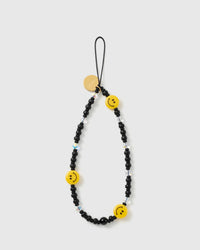 Matte black smiley bead phone strap laid flat, three yellow smiley beads and faceted clear accents on a black loop with a gold STICKYZOO disc.
