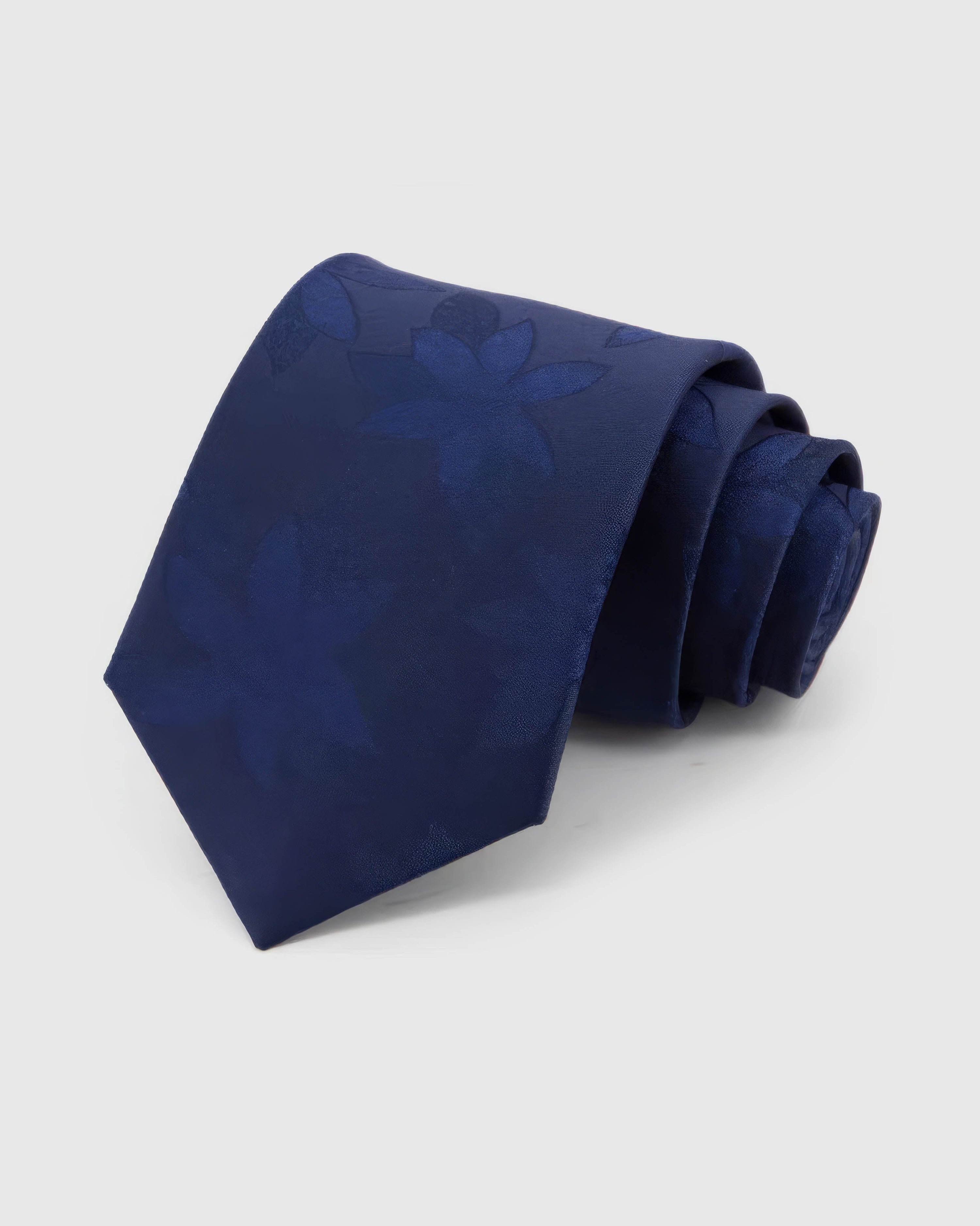 STICKYZOO Sapphire Tonal Bloom Tie rolled on white, showing a sapphire field with oversized tonal flower silhouettes and soft botanical forms across the front blade.