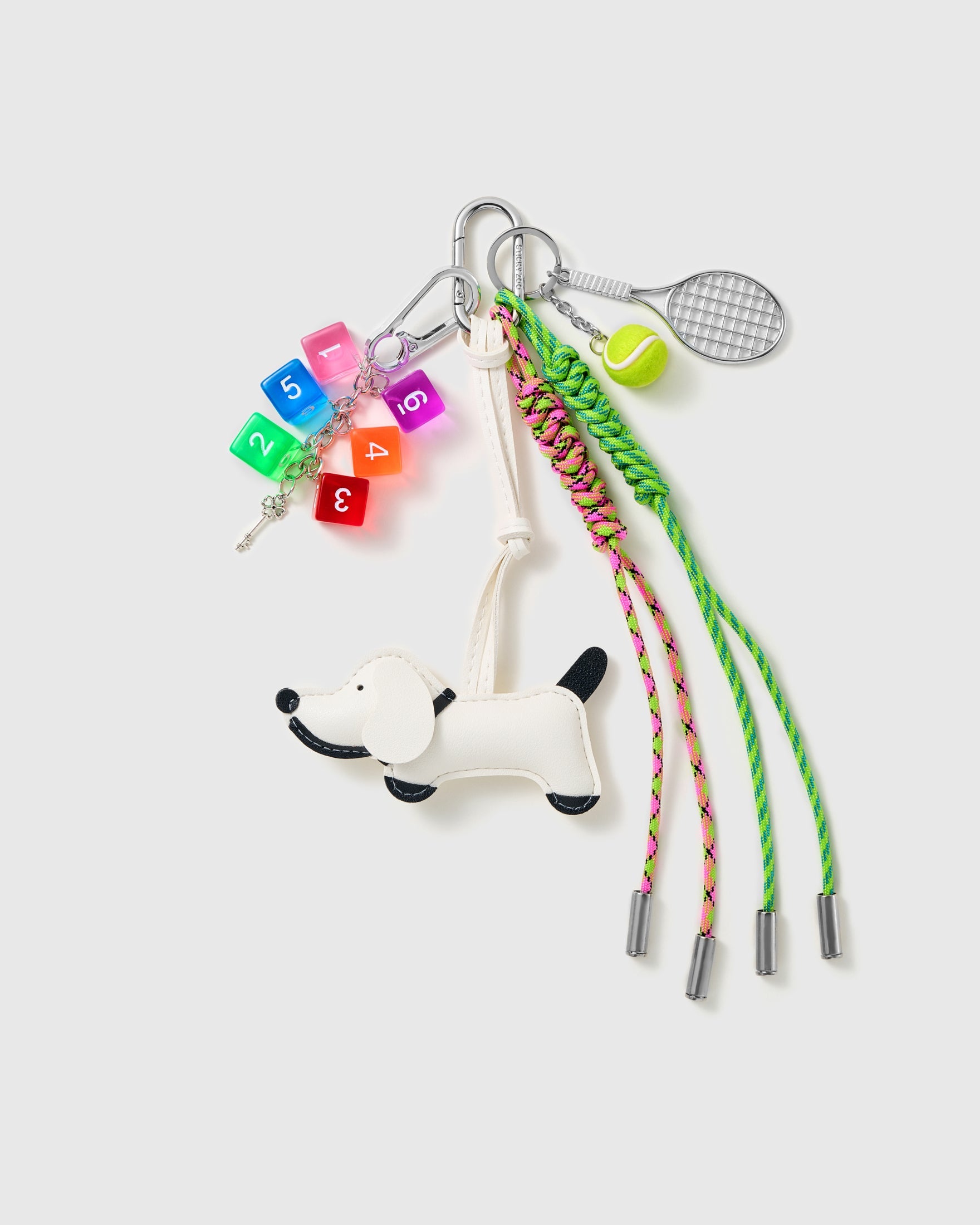 Tennis Pup Stack Charm with a white pup, tennis motifs, number blocks and green braided cords on a light background