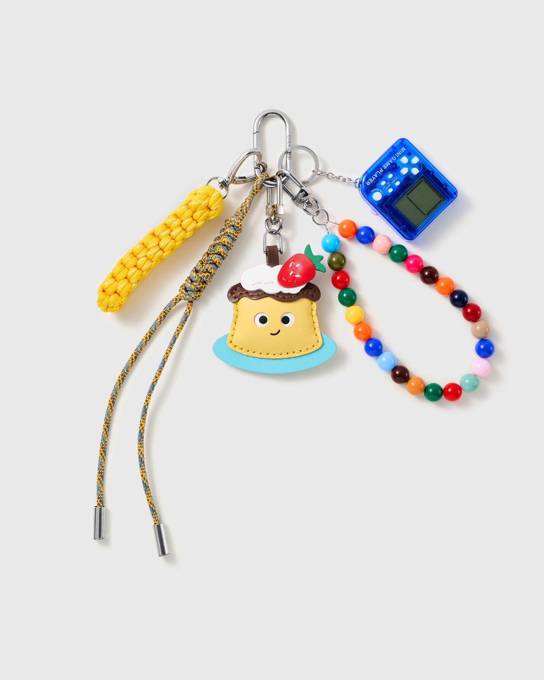 Arcade Cake Bead Stack Charm with a cake slice, blue handheld-game motif, multicolour bead loop and yellow cords on a light background