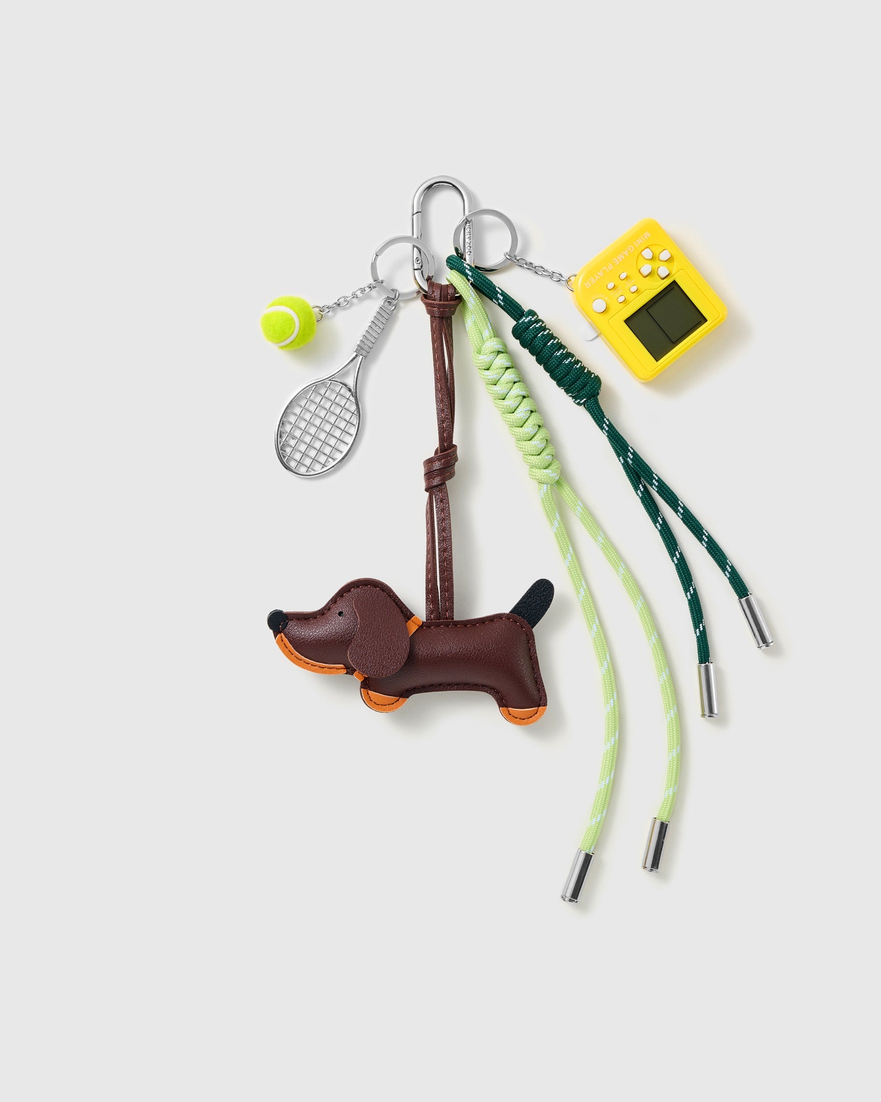 Dachshund Tennis Stack Charm with a brown dachshund, tennis motifs and green-and-brown cords on a light background
