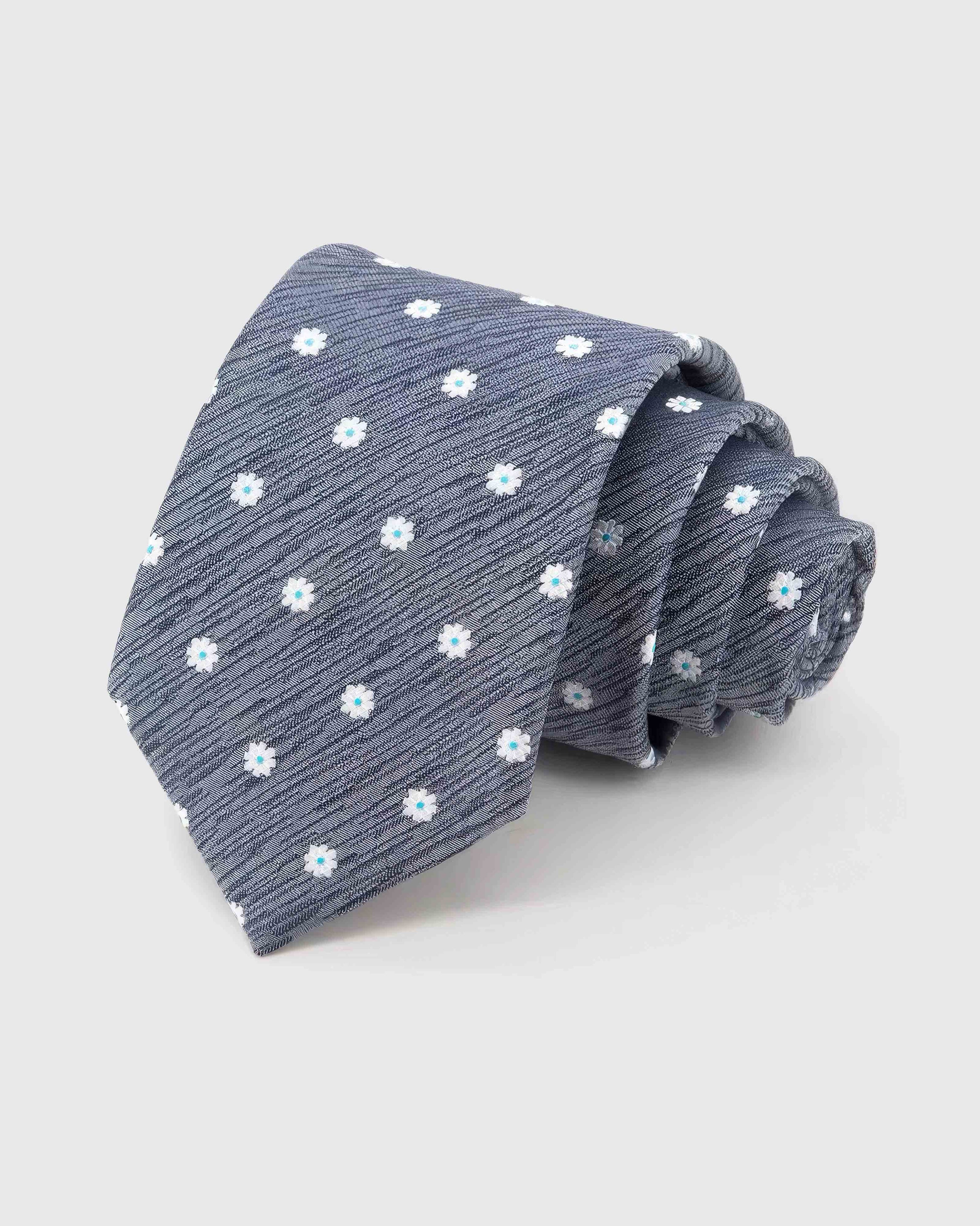 STICKYZOO Slate Daisy Tie rolled on white, showing small daisy blossoms across 100% mulberry silk in slate grey