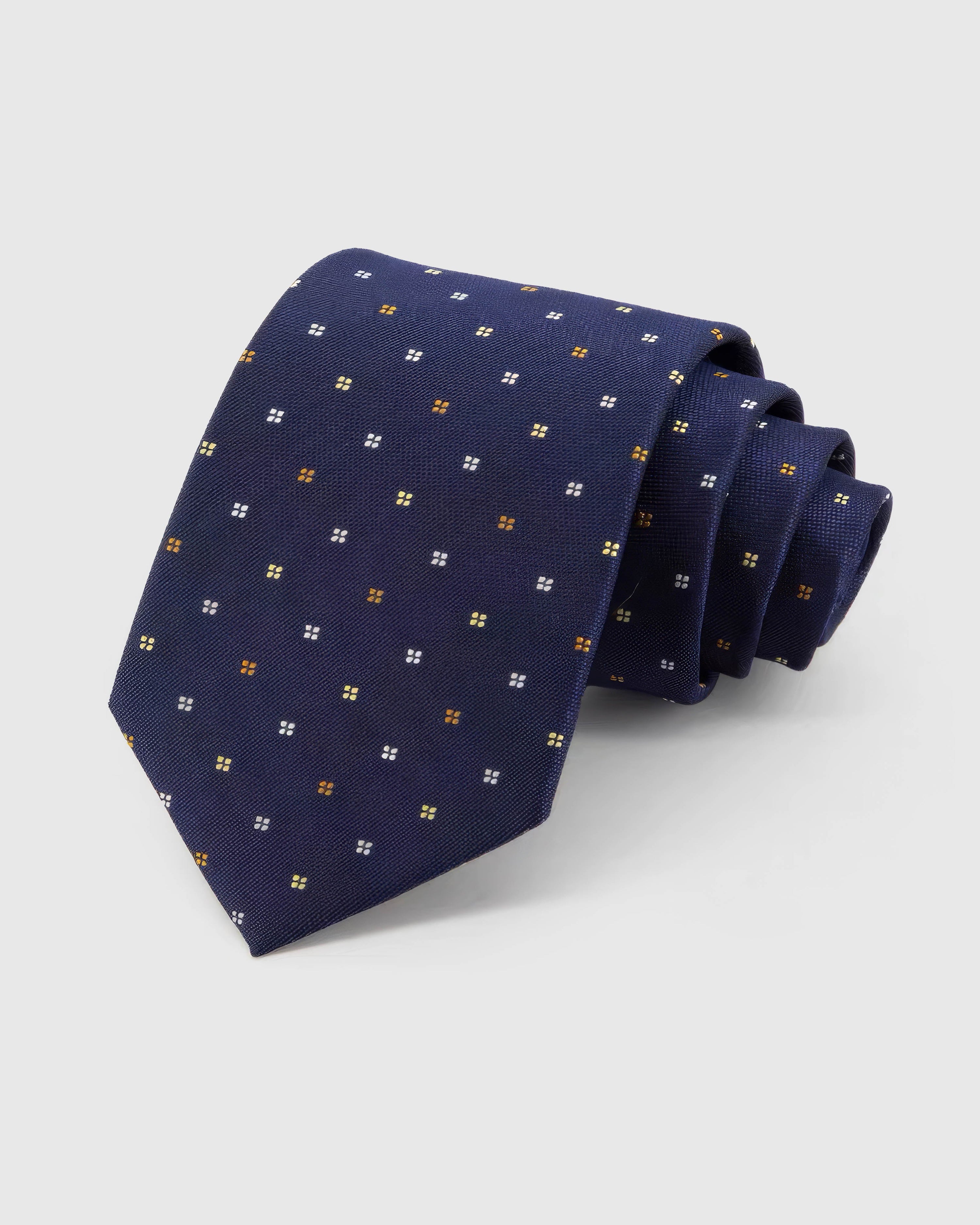 STICKYZOO Midnight Quatrefoil Tie rolled on white, showing gold, amber and ivory quatrefoils across 100% mulberry silk in midnight navy