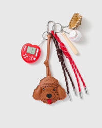 Cocoa Poodle Game Stack Charm with a cocoa-brown poodle face, red handheld-game motif, baseball details and red-and-brown cords on a light background