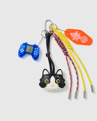Tuxedo Cat Game Stack Charm with a tuxedo-cat face, blue game-controller motif, stitched tag and yellow-and-blue cords on a light background