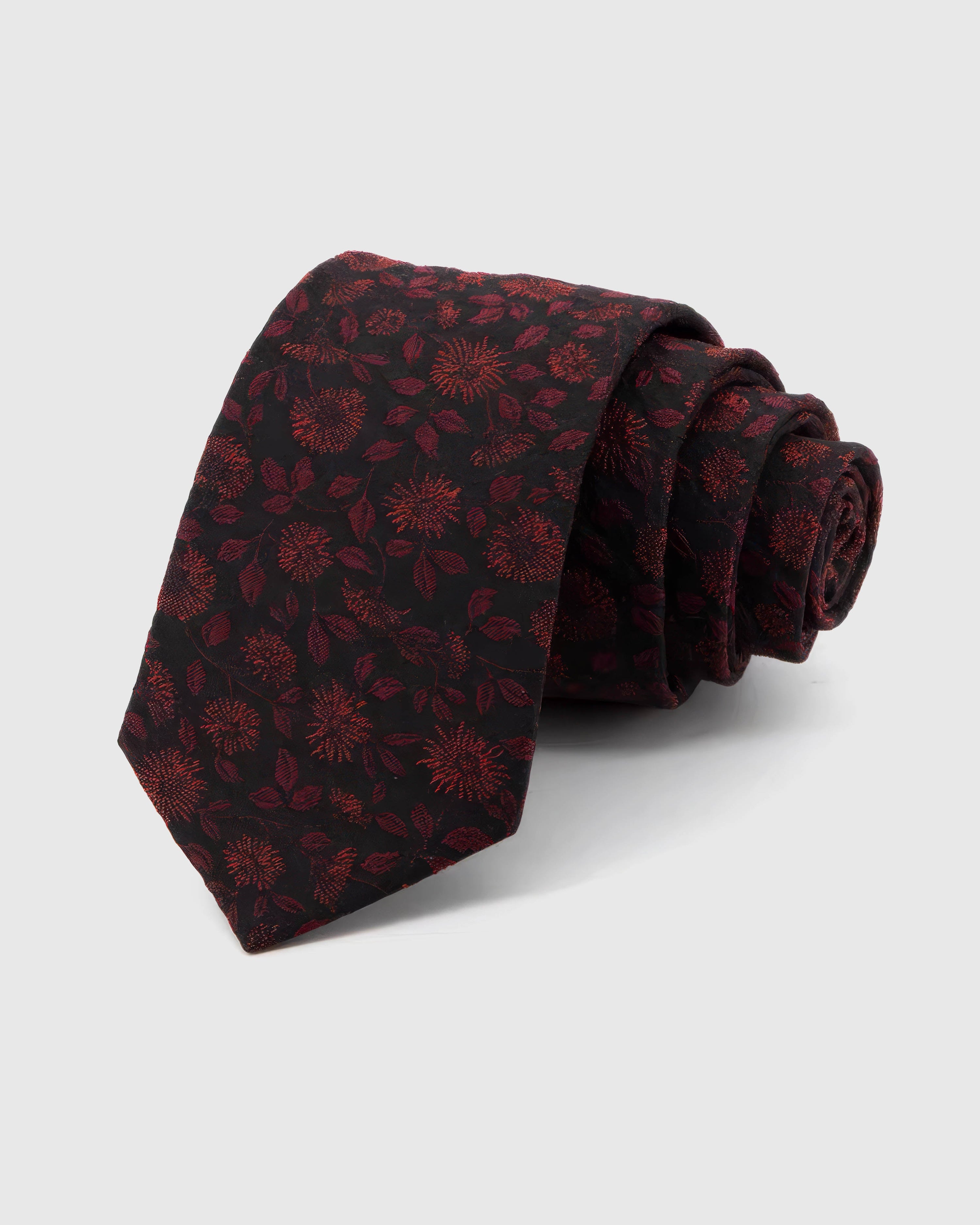 STICKYZOO Noir Crimson Bloom Tie rolled on white, showing a dark ground layered with crimson botanical blooms and shadowed leaves across the front blade.