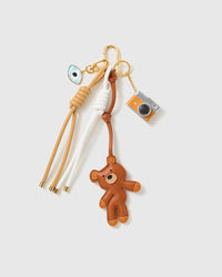 Teddy Evil Eye Camera Stack Charm with a brown teddy, evil-eye detail, miniature camera and cream-and-brown cords on a light background