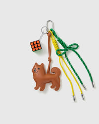Shiba Puzzle Stack Charm with a brown shiba-style pup, puzzle cube, green bow and yellow-and-green cords on a light background