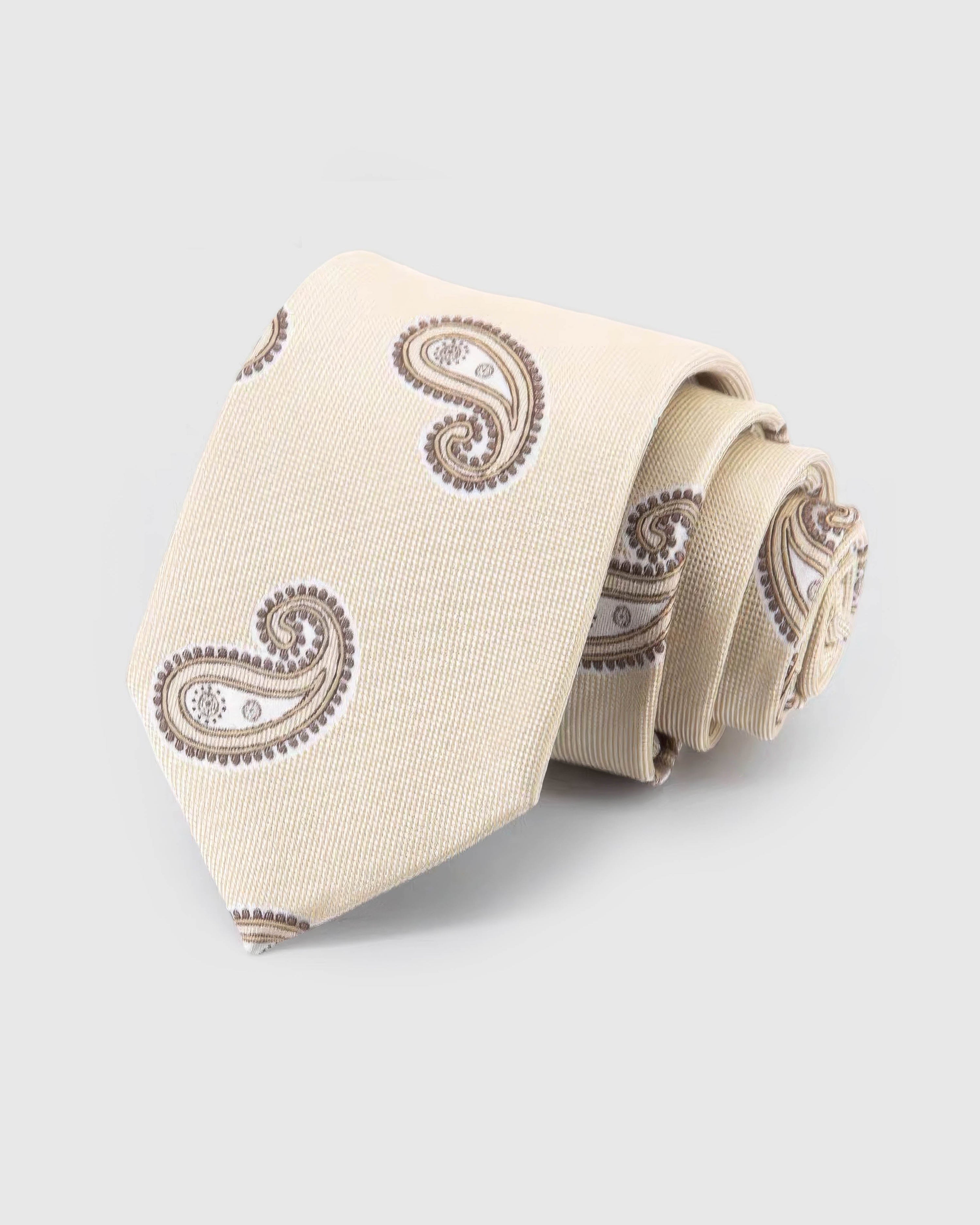 STICKYZOO Ivory Taupe Paisley Tie rolled on white, showing an ivory ground with widely spaced taupe and brown paisley forms across the front blade.