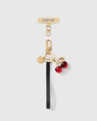 STICKYZOO black leather phone strap with a glossy red cherry charm, gold-tone leaf, engraved disc and gold Phone Strap Card tab.
