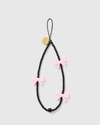 STICKYZOO Midnight Bow phone strap laid flat: matte black beads, three glossy pink bows, one black bead, a black cord loop and gold disc.