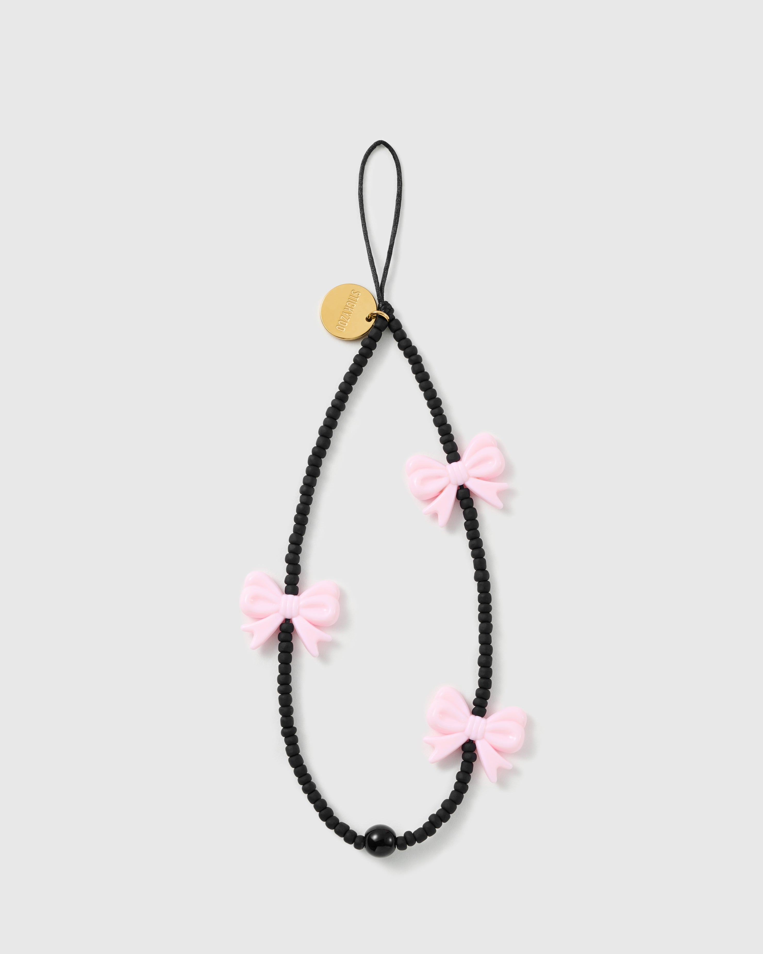STICKYZOO Midnight Bow phone strap laid flat: matte black beads, three glossy pink bows, one black bead, a black cord loop and gold disc.