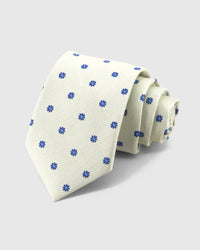 STICKYZOO Ivory Cobalt Bloom Tie rolled on white, showing cobalt eight-petal blooms across 100% mulberry silk in ivory cream