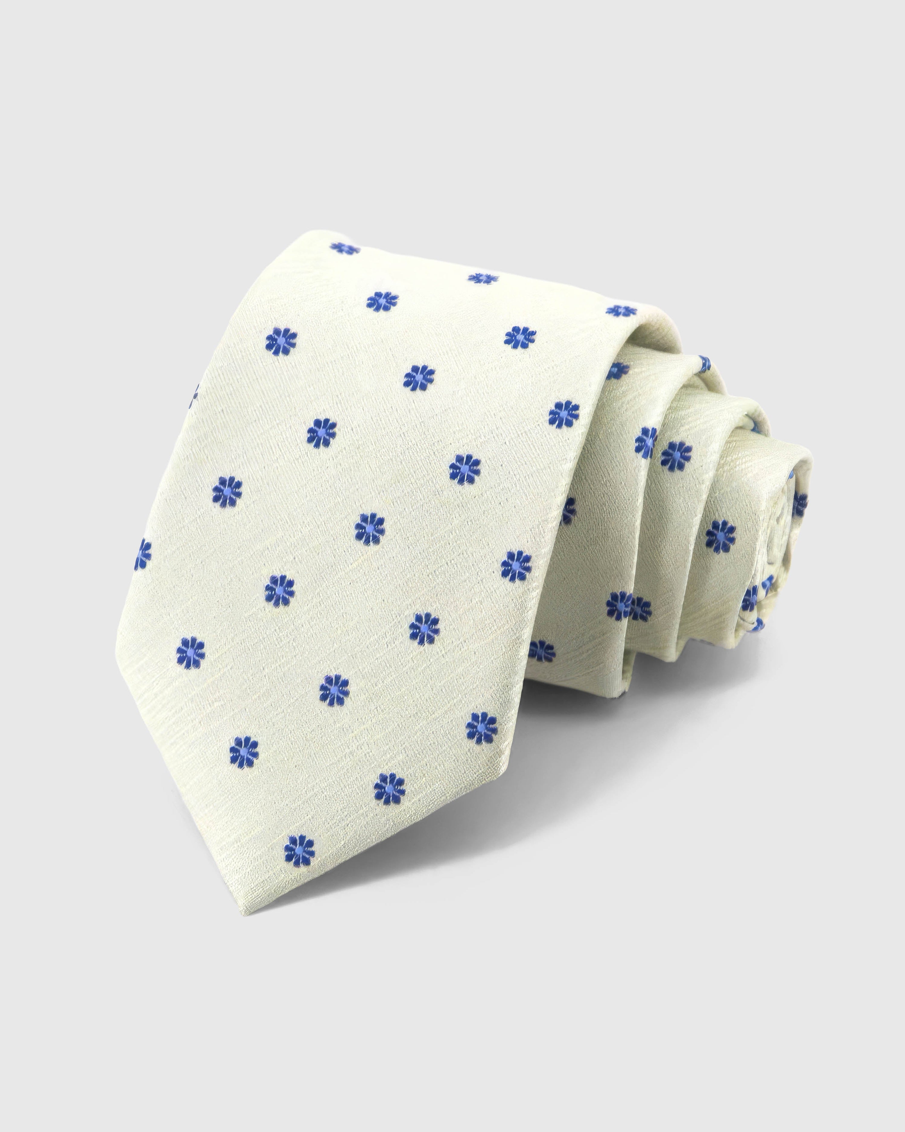 STICKYZOO Ivory Cobalt Bloom Tie rolled on white, showing cobalt eight-petal blooms across 100% mulberry silk in ivory cream