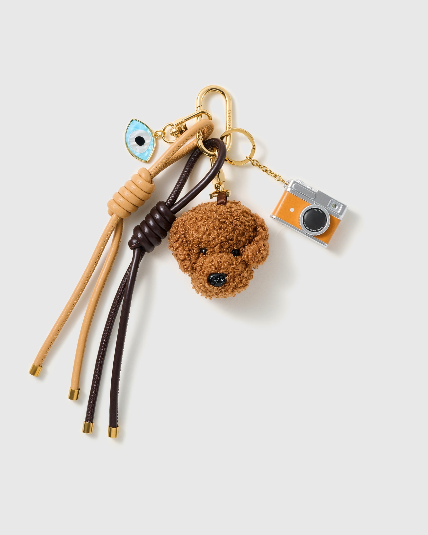 Poodle Evil Eye Camera Stack Charm with a brown poodle face, evil-eye detail, miniature camera and brown-and-cream cords on a light background