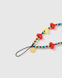 Close-up of the black stretch-cord loop and gold STICKYZOO disc beside glossy red and yellow hearts and rainbow-striped beads.