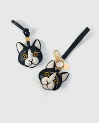 Both editions of the tuxedo cat side by side — leather strap loop for bags, or 18K gold-plated keychain clip with engraved disc.