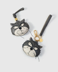 Both editions of the Grump cat side by side — leather strap loop for bags, or 18K gold-plated keychain clip with engraved disc.