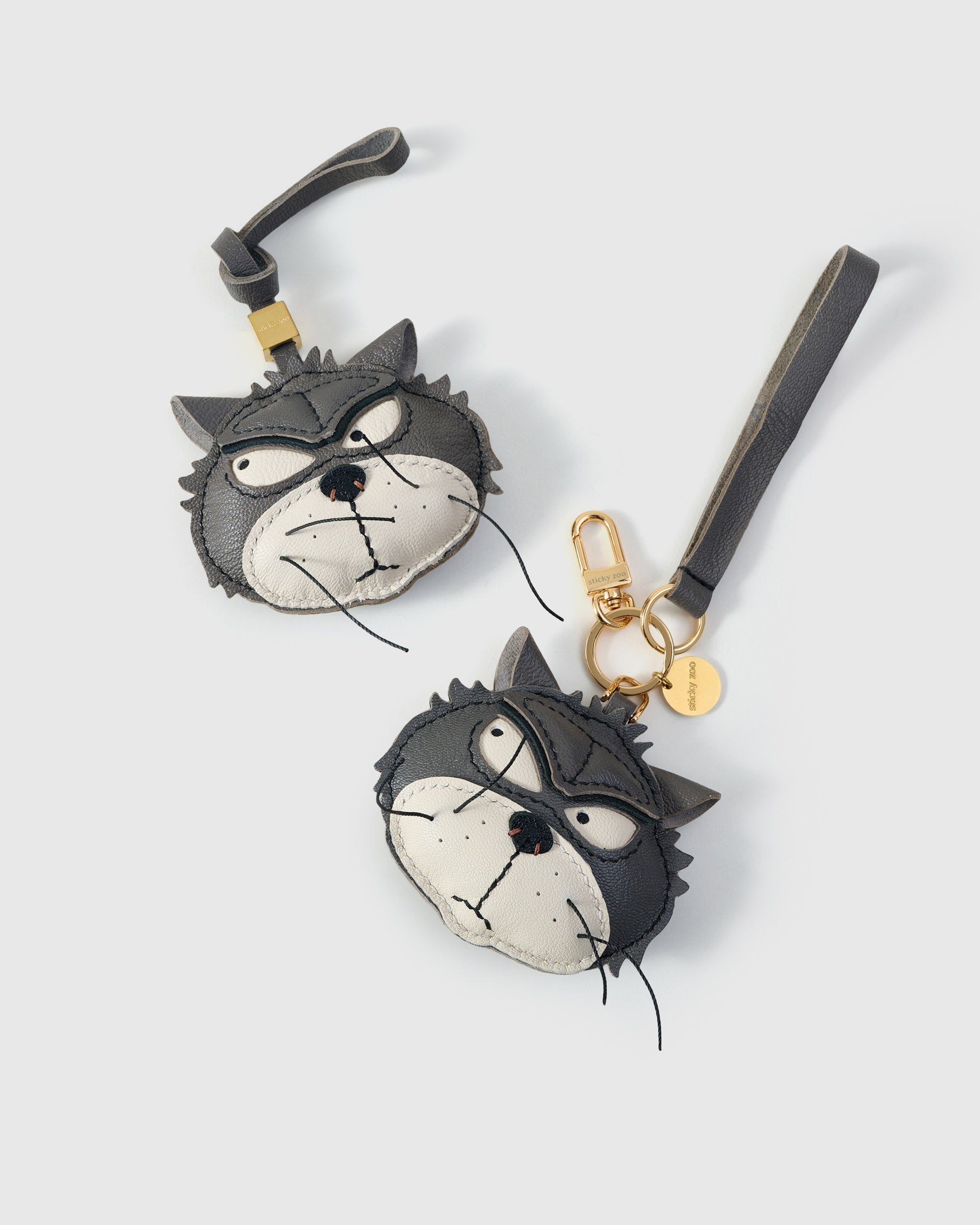 Both editions of the Grump cat side by side — leather strap loop for bags, or 18K gold-plated keychain clip with engraved disc.