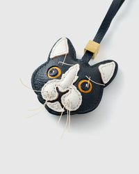 Tight close-up of the tuxedo cat face — gold-yellow eyes in real leather, white face mask, real fiber whiskers stitched in. Every panel by hand.