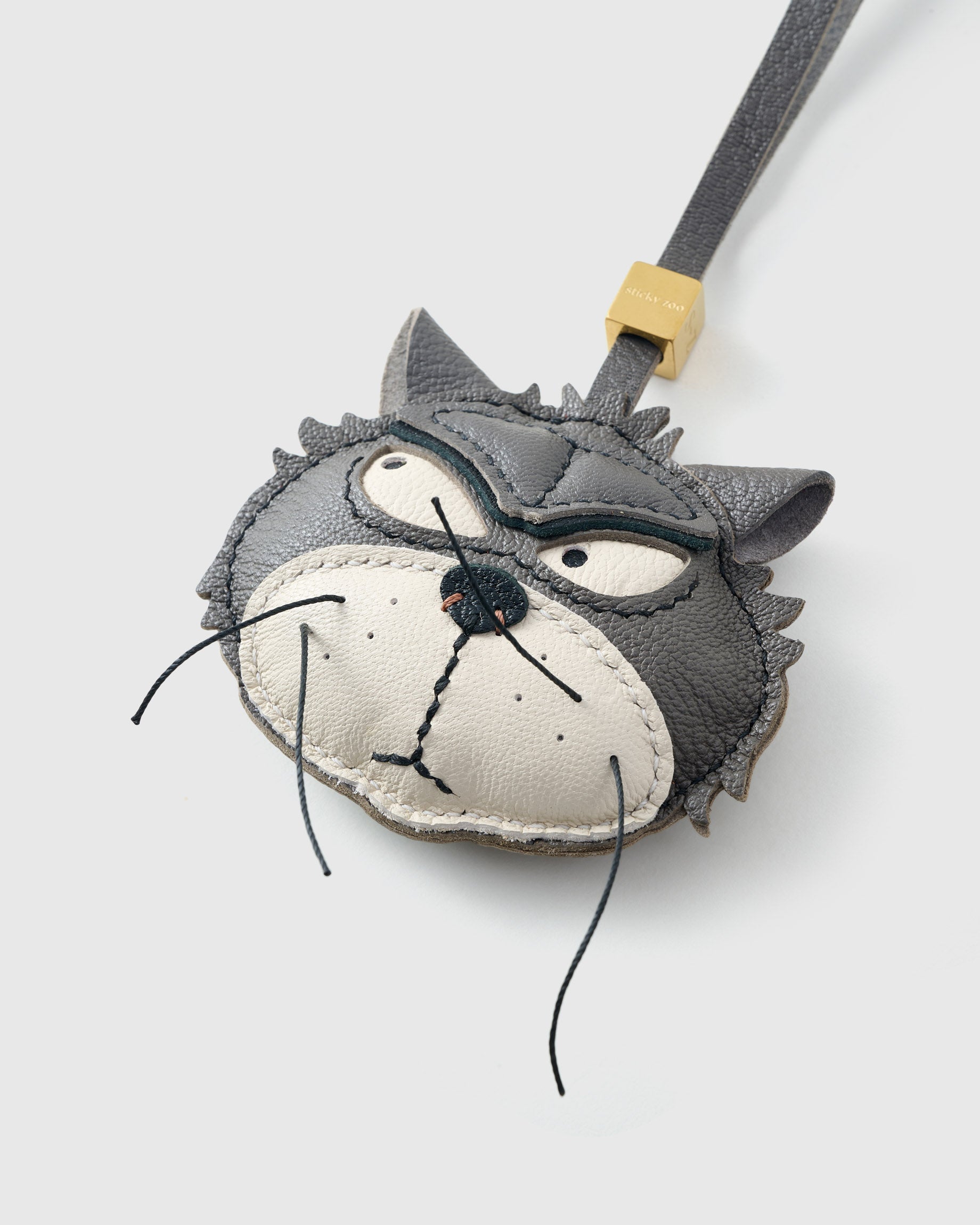 Tight close-up of the Grump cat face, angled — gold-orange eyes in real leather, dark masked markings, real fiber whiskers. Every panel by hand.