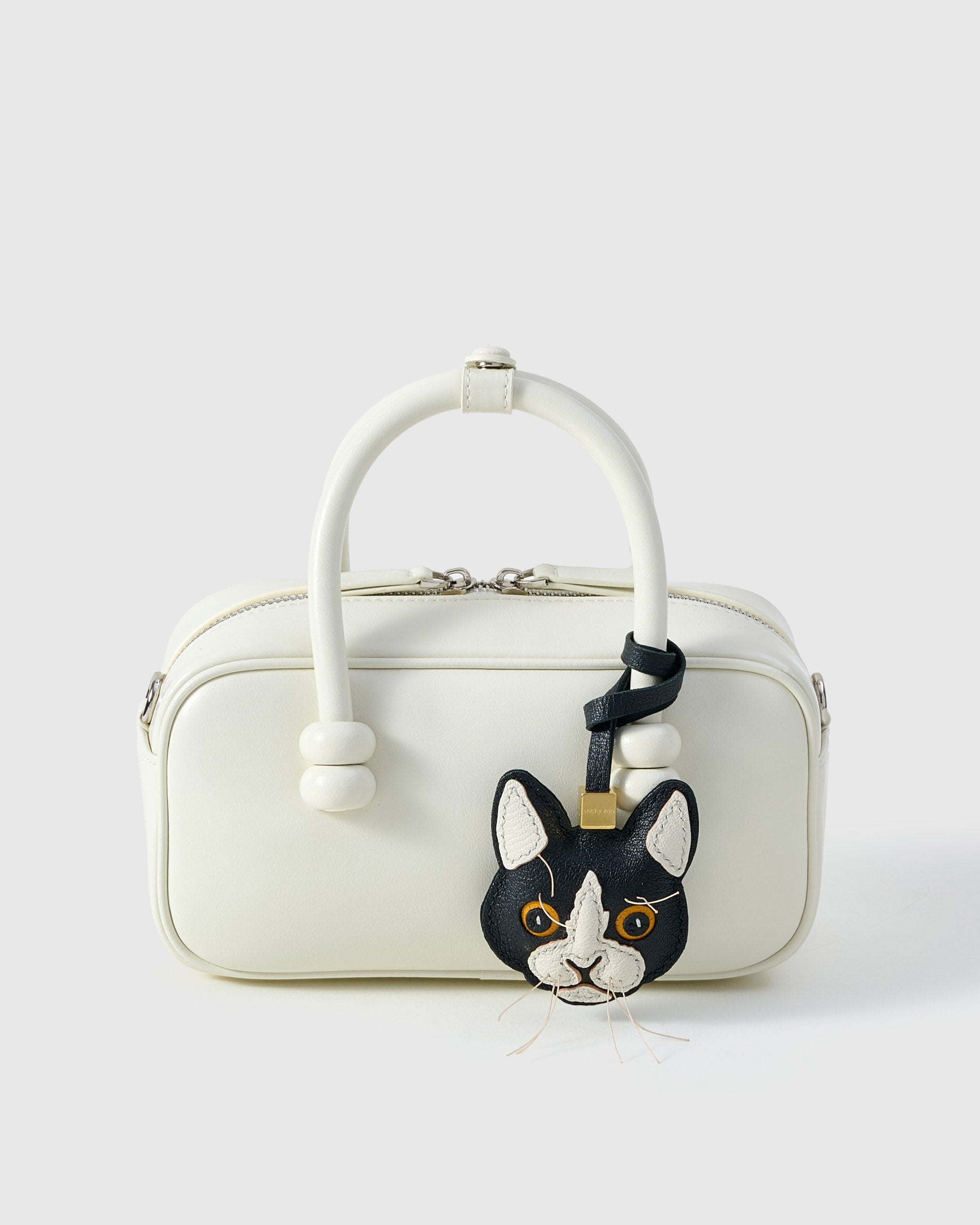 Tuxedo cat charm styled on a cream box bag, front — a small, specific piece that turns a simple bag into a personal one.