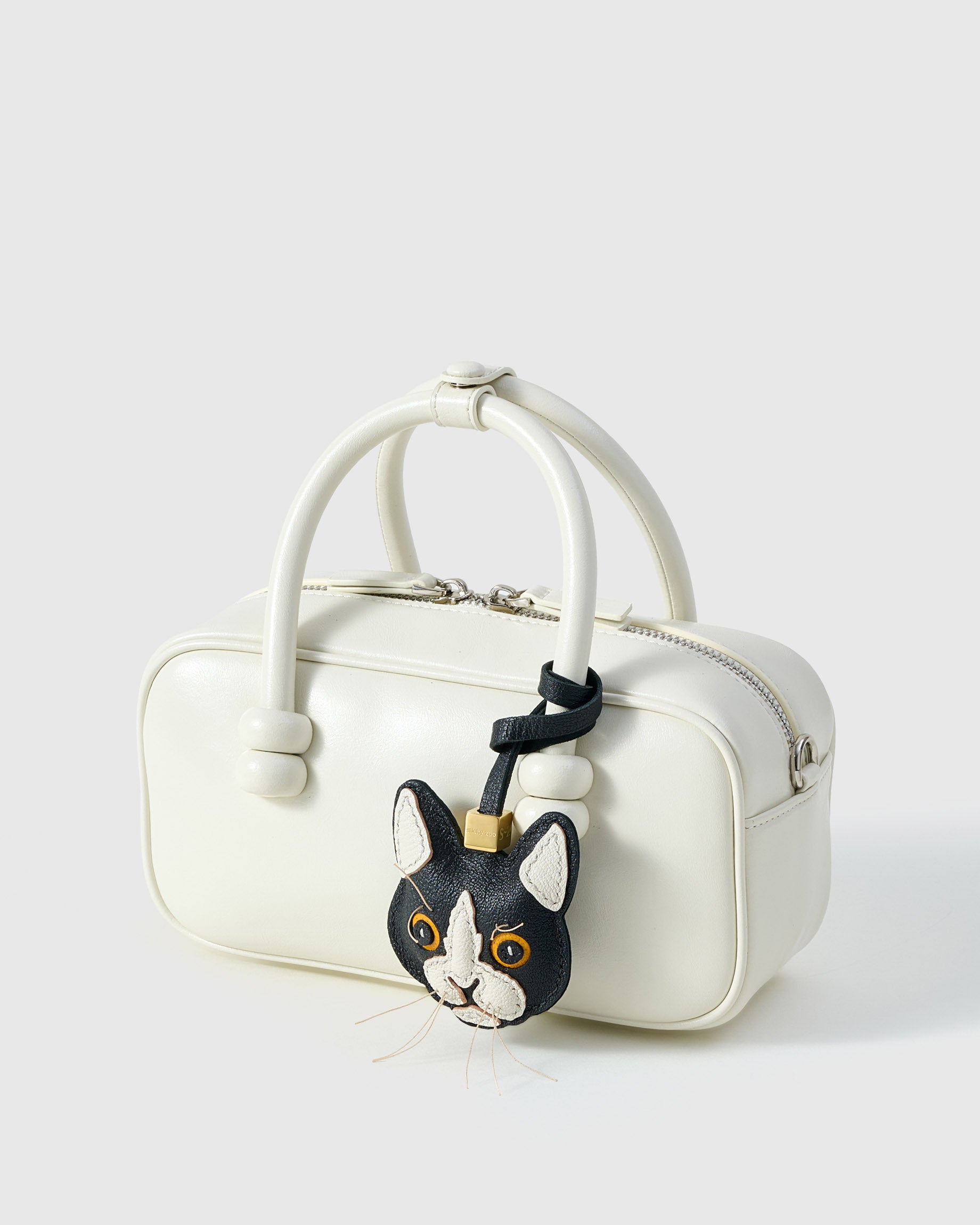 Tuxedo cat charm on a cream box bag, side angle — Real French leather, 3 days by hand.