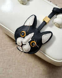 Tuxedo cat charm hanging on a cream box bag, close detail — every fiber whisker stitched into the real French Alran goatskin face by hand.