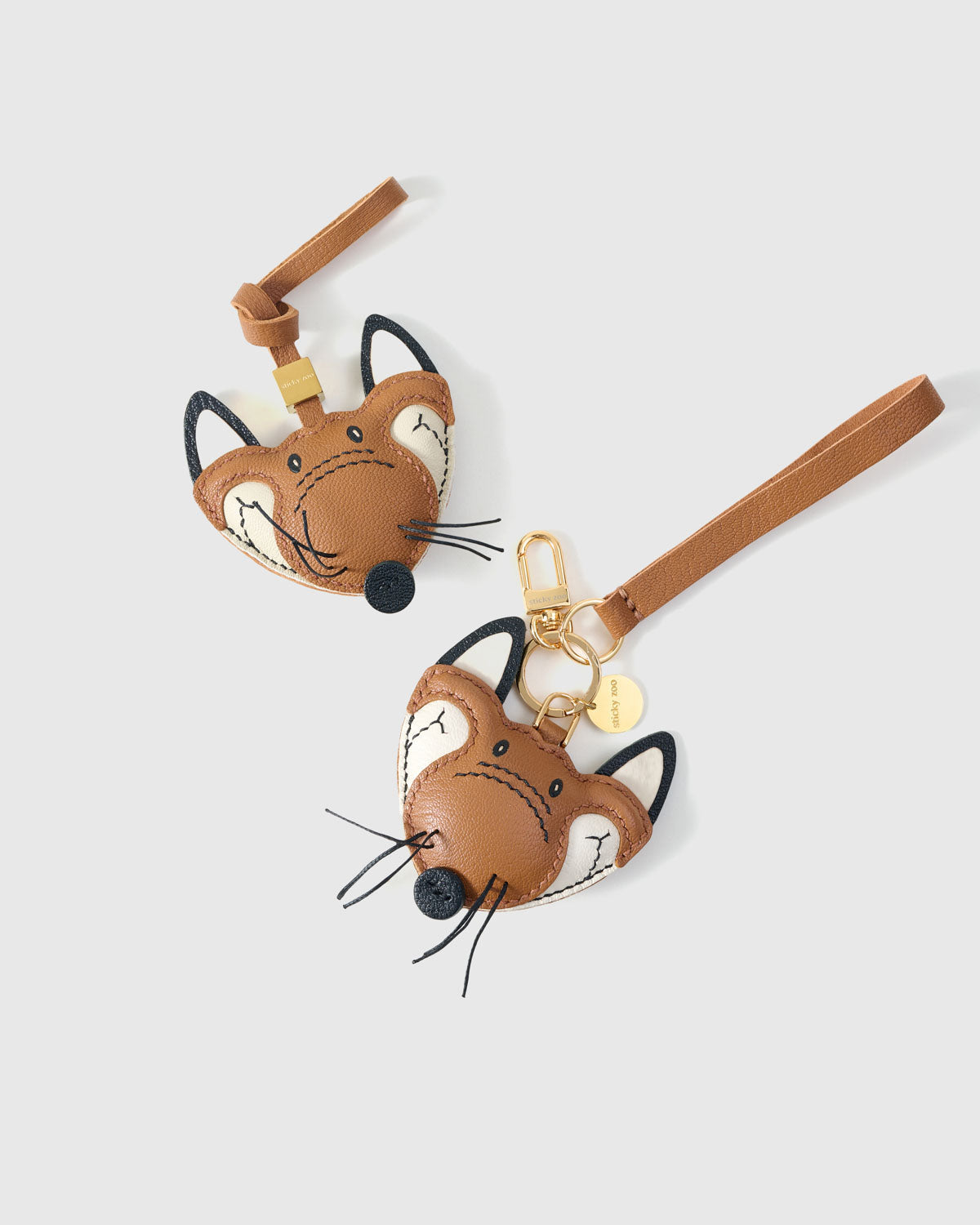 Both editions of the fox charm — leather strap loop for bags, or 18K gold-plated keychain clip.