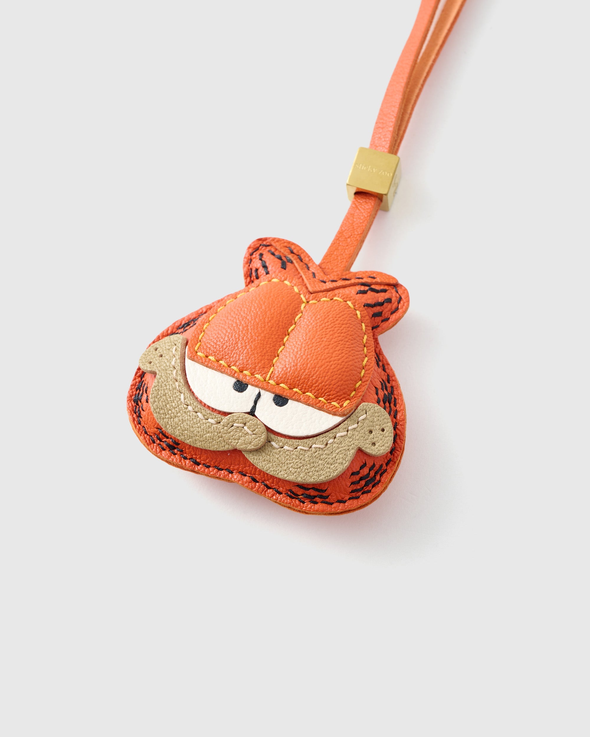 Both editions of the Garfield charm — leather strap loop for bags, or 18K gold-plated keychain clip.